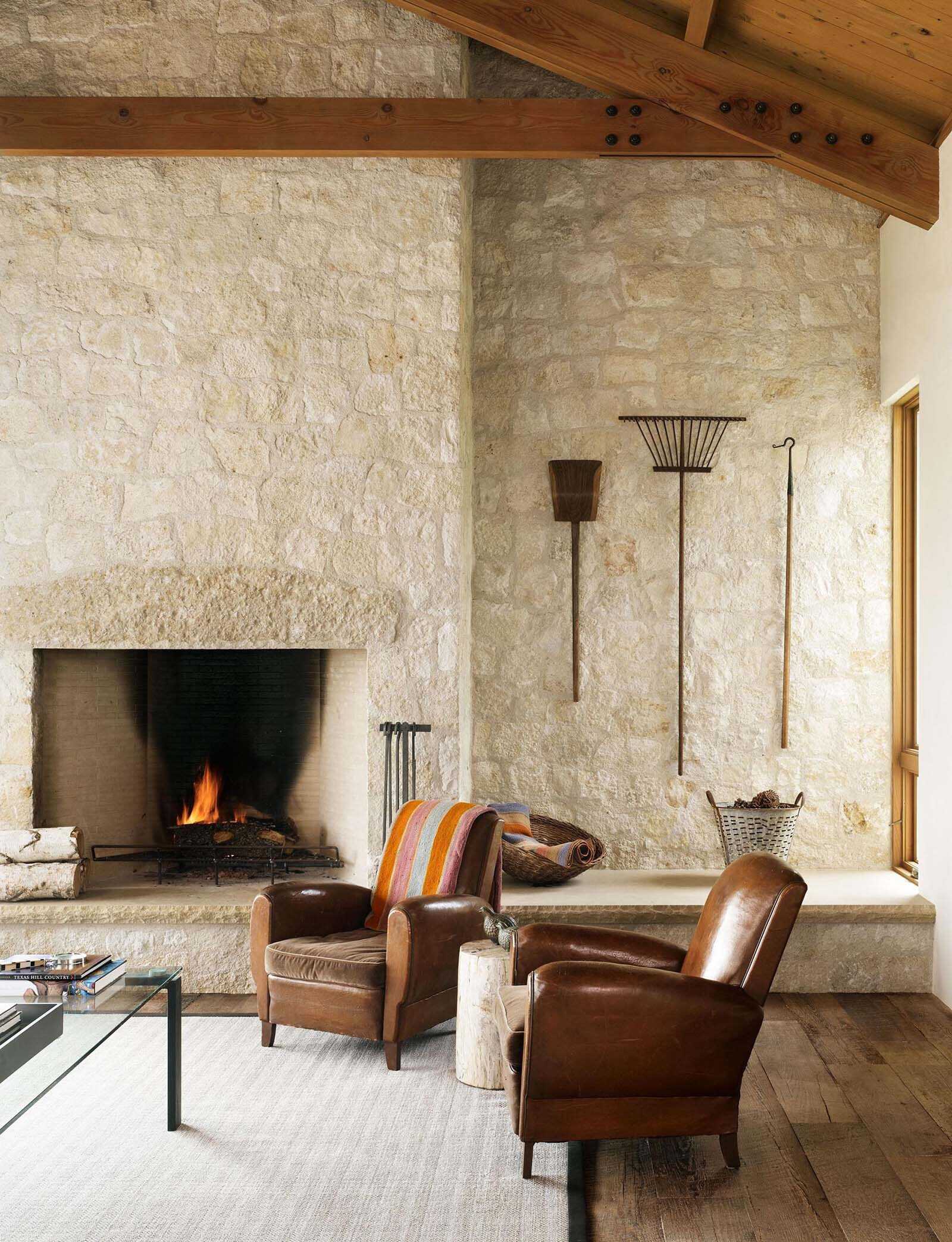 A living room where limestone walls meet exposed wood trusses, creating a warm and textured interior anchored by a stone fireplace.