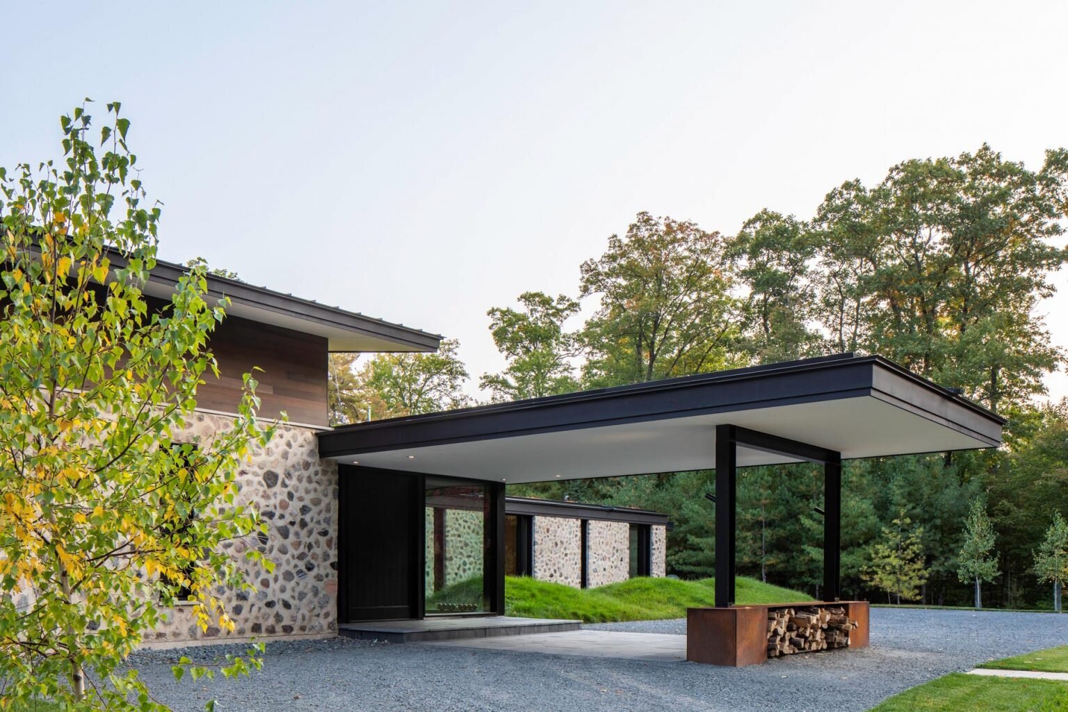 Una entrada cubierta con puertas pivotantes de madera personalizadas marca el tono de esta moderna casa de huéspedes frente al lago en Wisconsin.