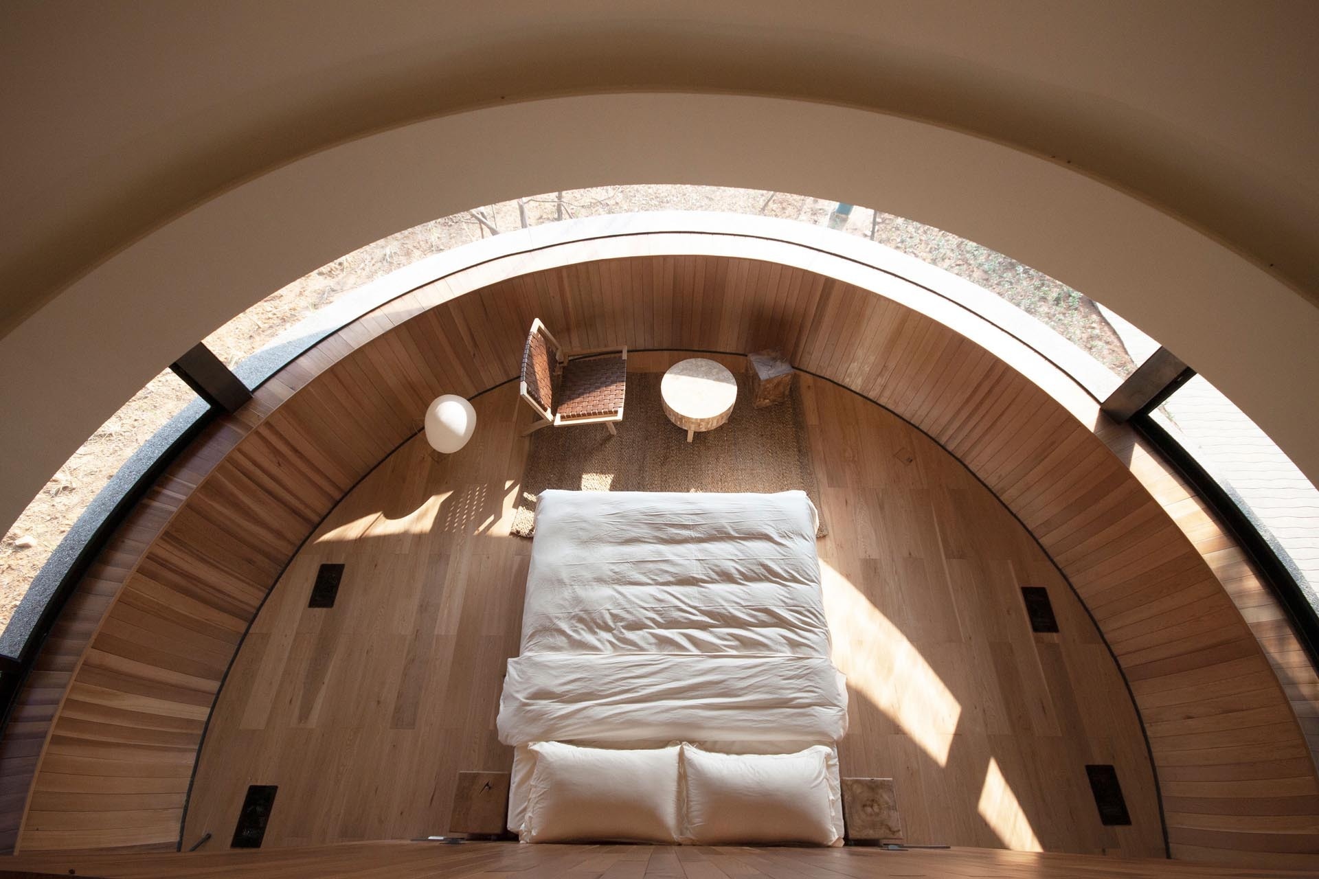 Curved panoramic windows wrap the bedroom, framing uninterrupted views of the surrounding pine forest.