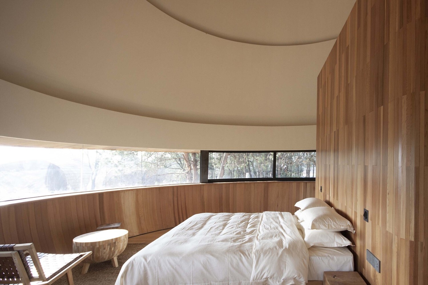 Curved panoramic windows wrap the bedroom, framing uninterrupted views of the surrounding pine forest.