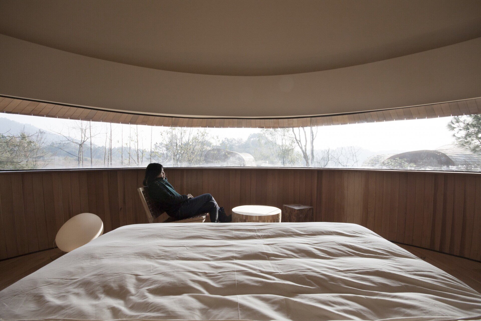 Curved panoramic windows wrap the bedroom, framing uninterrupted views of the surrounding pine forest.