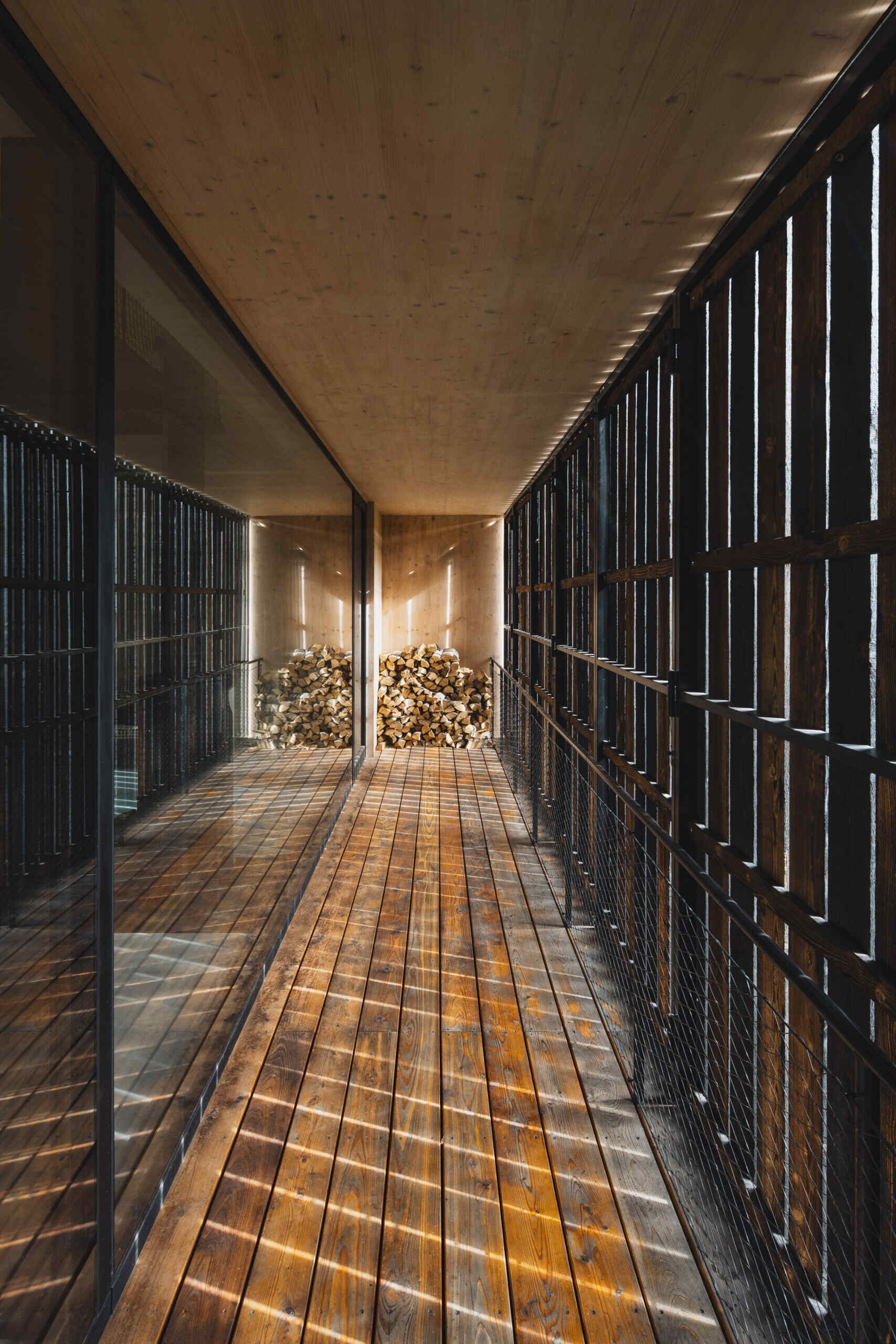 A full-height living space with floor-to-ceiling glazing connects seamlessly to a raised terrace overlooking the river. Shutters are used to enclose the terrace.