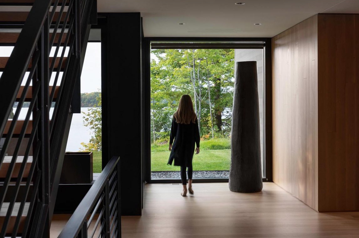 Una entrada cubierta con puertas pivotantes de madera personalizadas marca el tono de esta moderna casa de huéspedes frente al lago en Wisconsin.