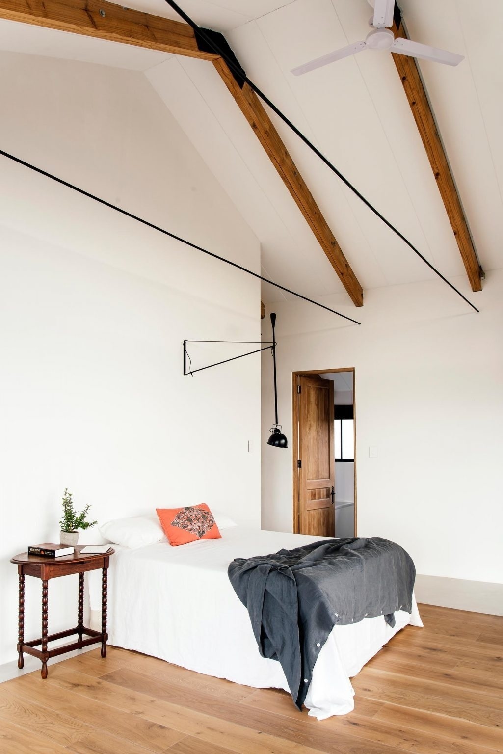 A minimal bedroom opens to tree canopy views, with shutters and overhangs controlling sunlight.