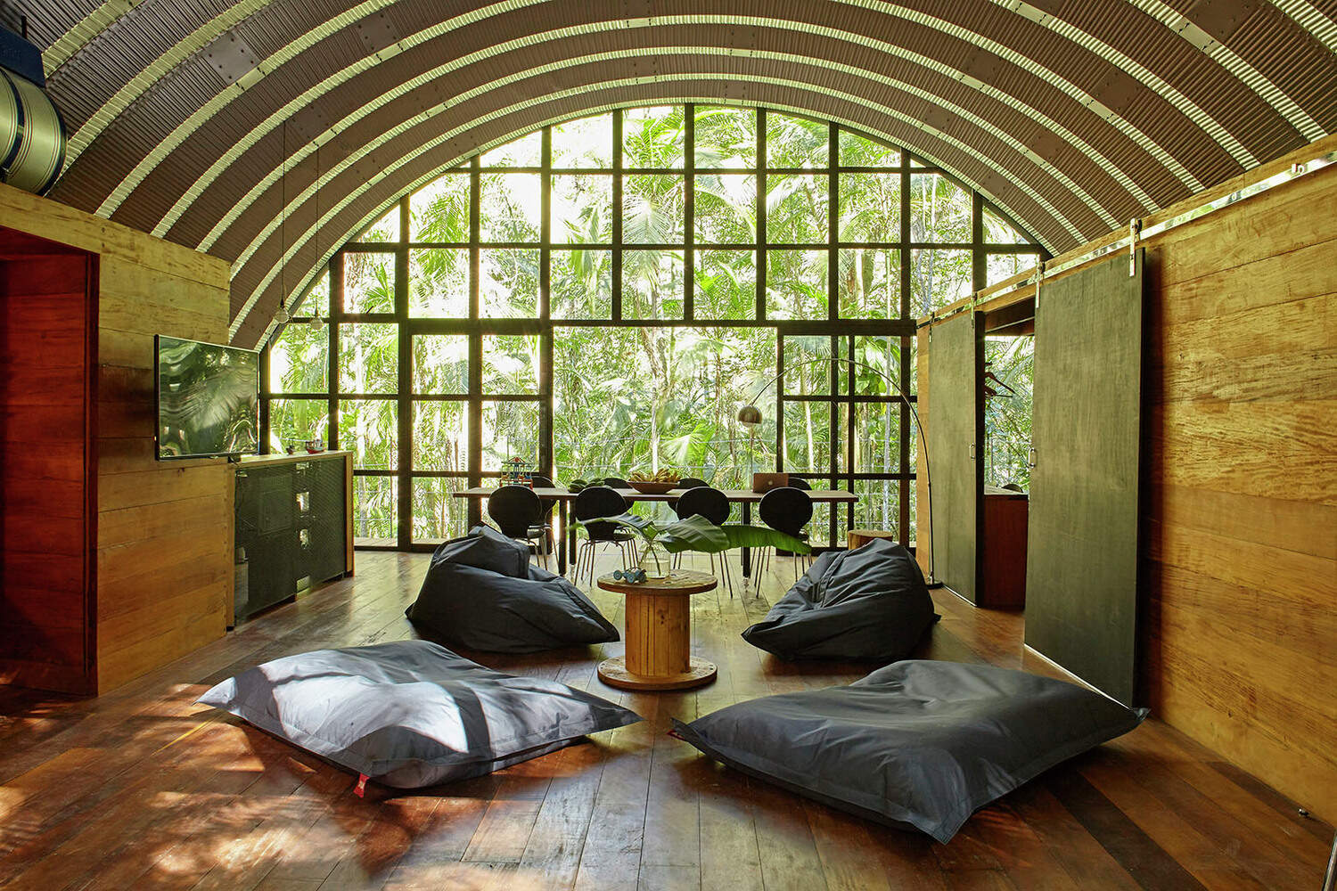 An open-plan interior where kitchen, dining, and living areas sit beneath one continuous curved roof.