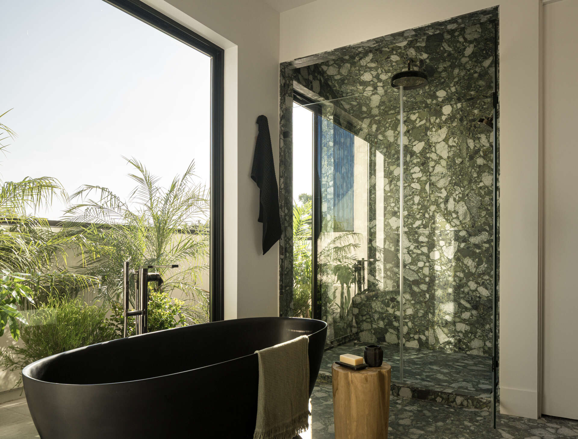 In this bathrooms, the black freestanding bathtub immediately draws attention, set against a backdrop of richly patterned stone that wraps the shower walls and floor. Positioned beside the windows, the bath and shower takes full advantage of natural light and views of greenery just outside.