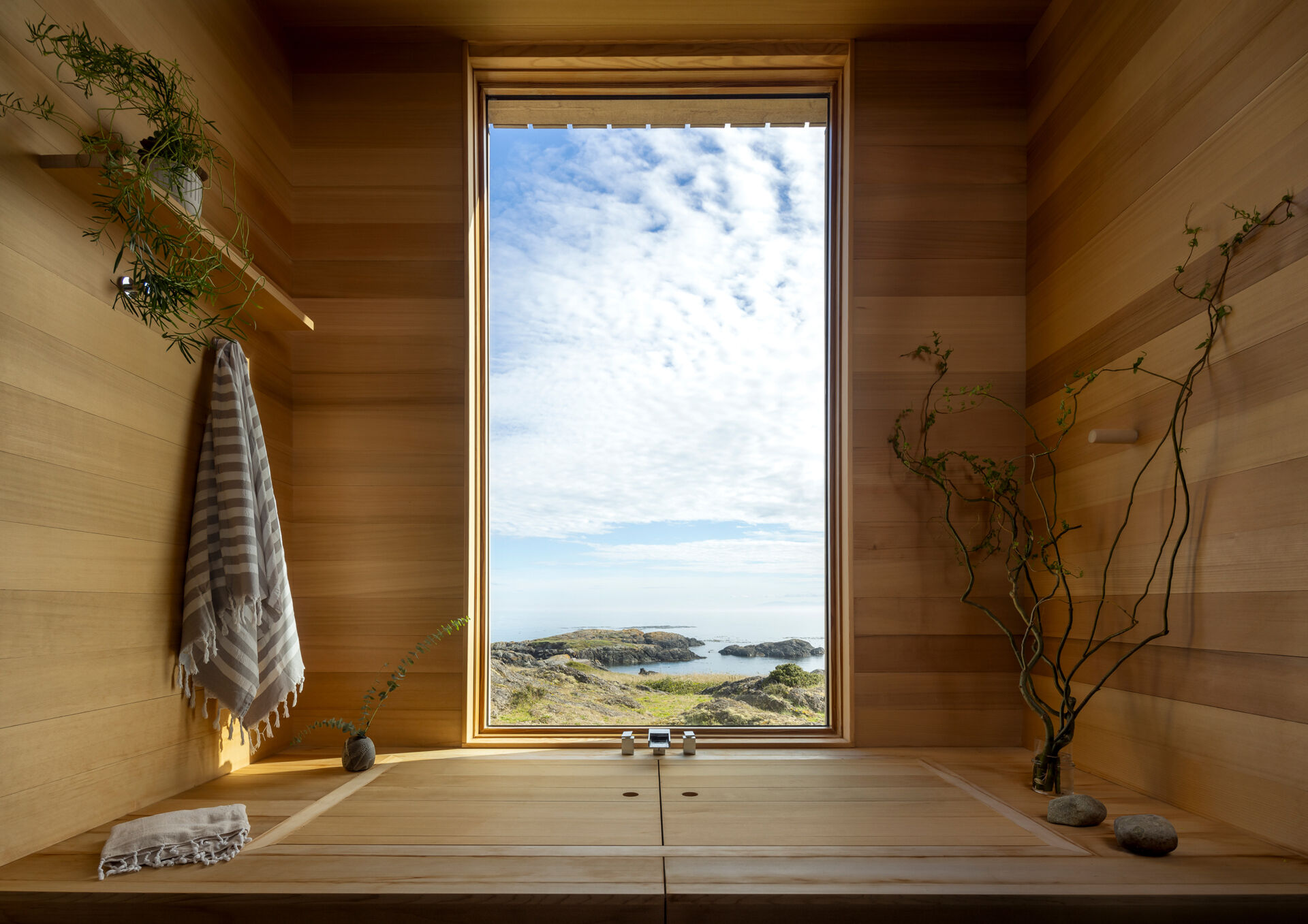 The bathroom continues the same material palette found throughout the home, with a built-in soaking tub hidden beneath a wood cover and positioned beneath the window.