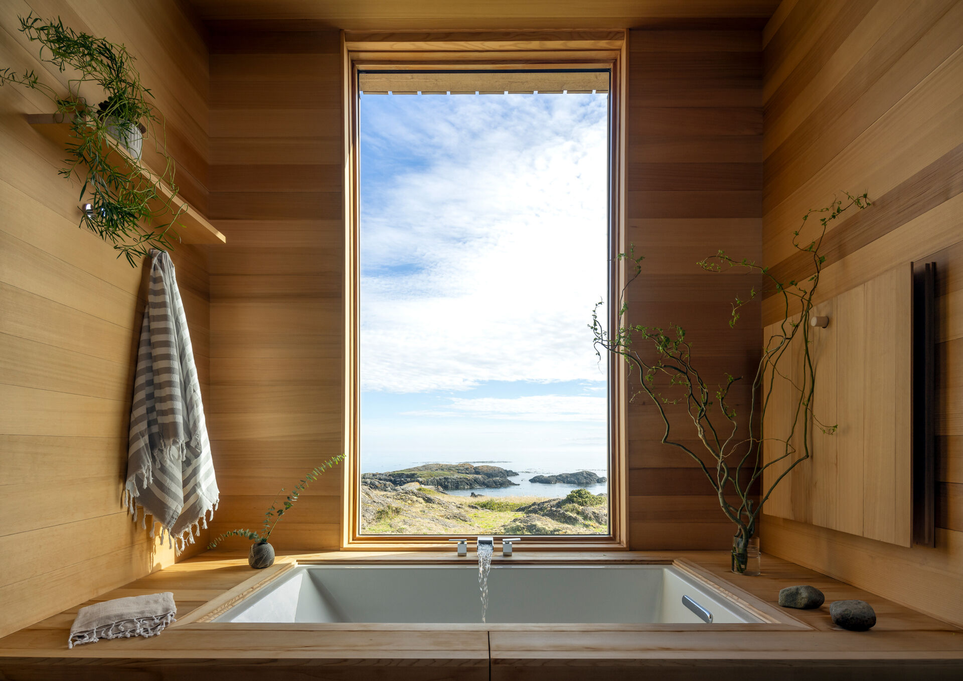 The bathroom continues the same material palette found throughout the home, with a built-in soaking tub hidden beneath a wood cover and positioned beneath the window.