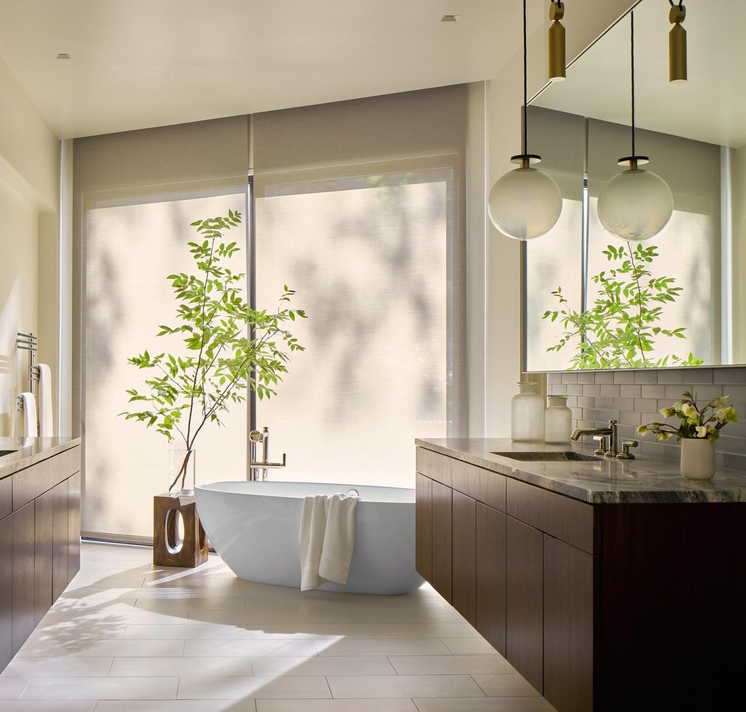 In this bathroom, dual vanities sit alongside a freestanding bathtub positioned near the windows, allowing light to filter in throughout the day.