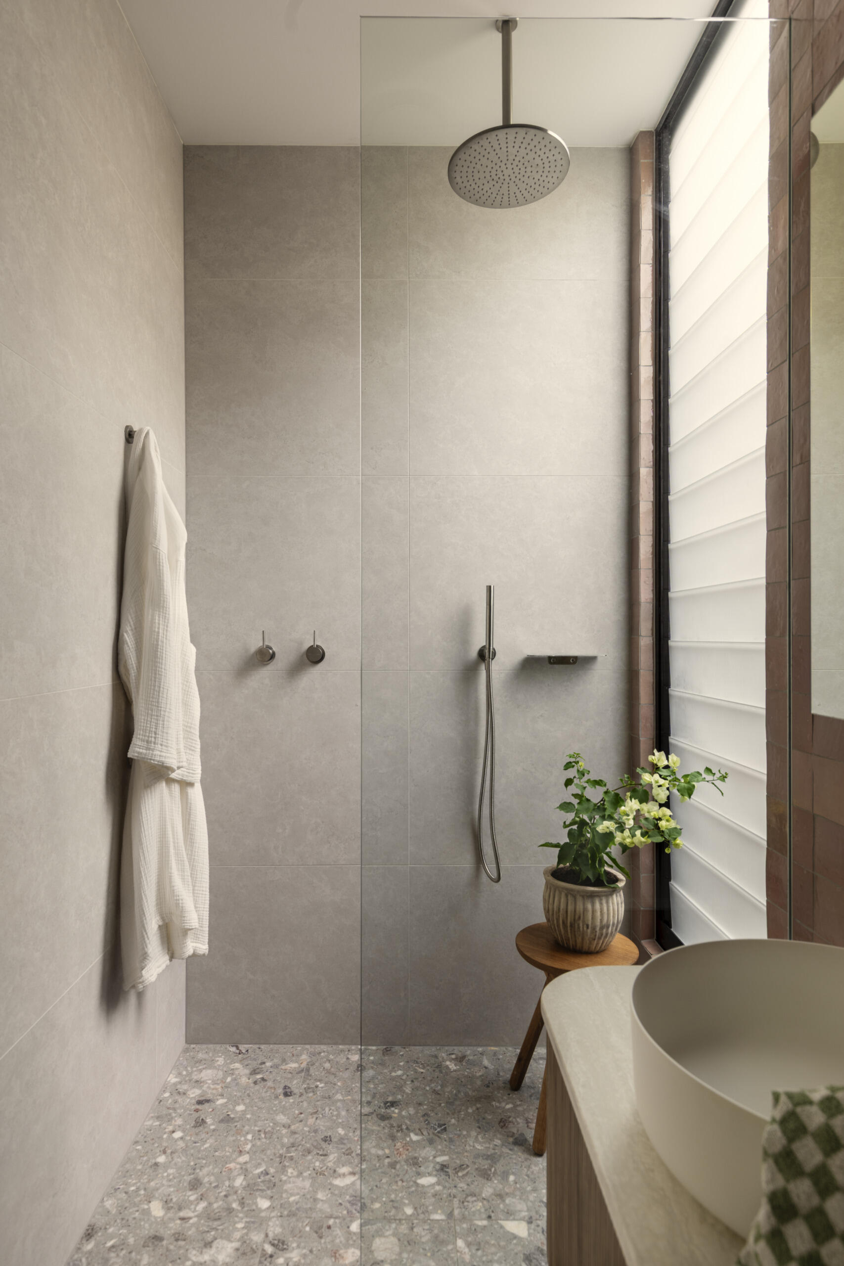 This guest bathroom sits nearby and pairs earthy terracotta-colored tile with soft gray surfaces for a look that feels warm and grounded. The ribbed wood vanity adds texture, while the round vessel sink keeps the lines clean and sculptural.