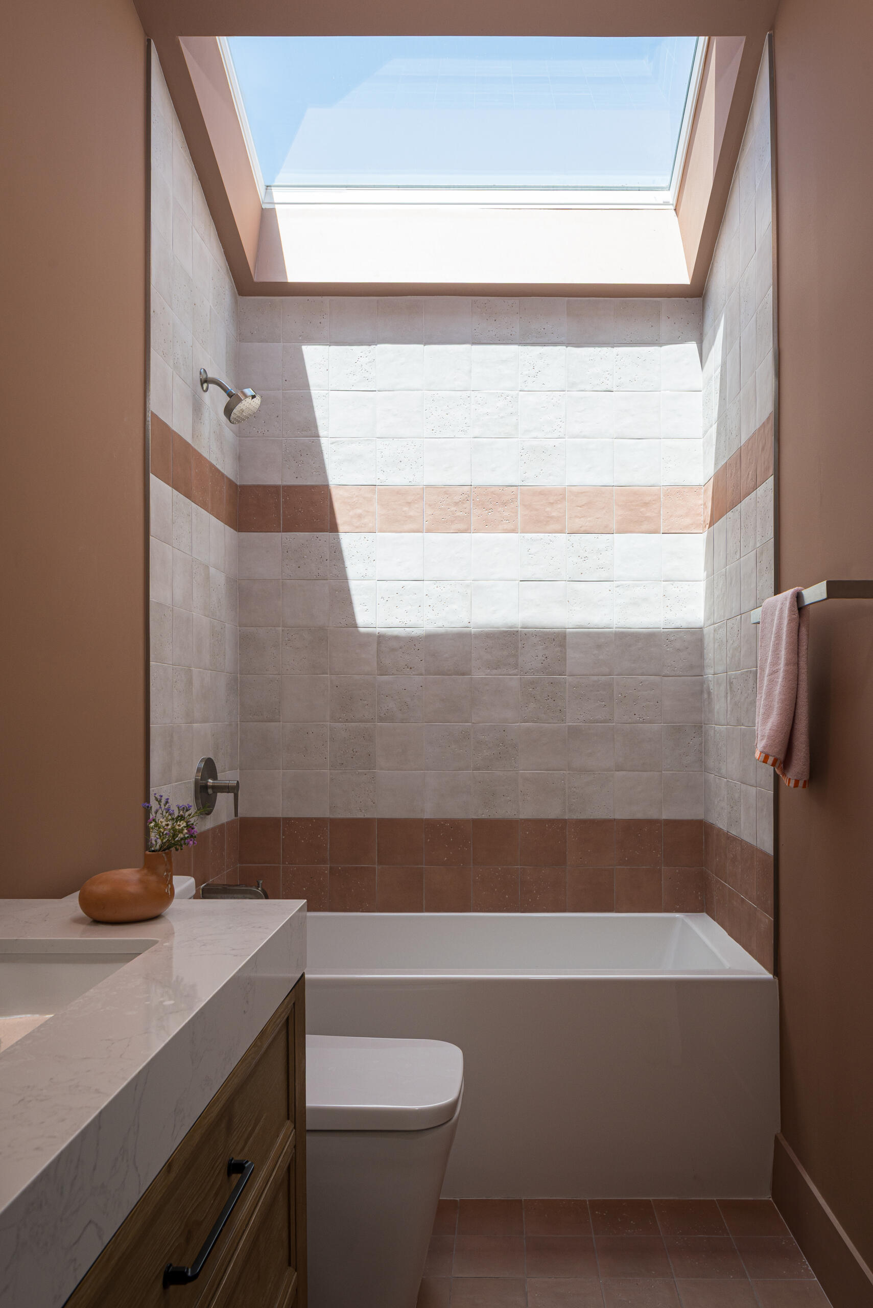 This bathroom uses a skylight positioned directly above a built-in bathtub and shower combination. This overhead light transforms the space, making it feel bright and open without relying on large windows.
