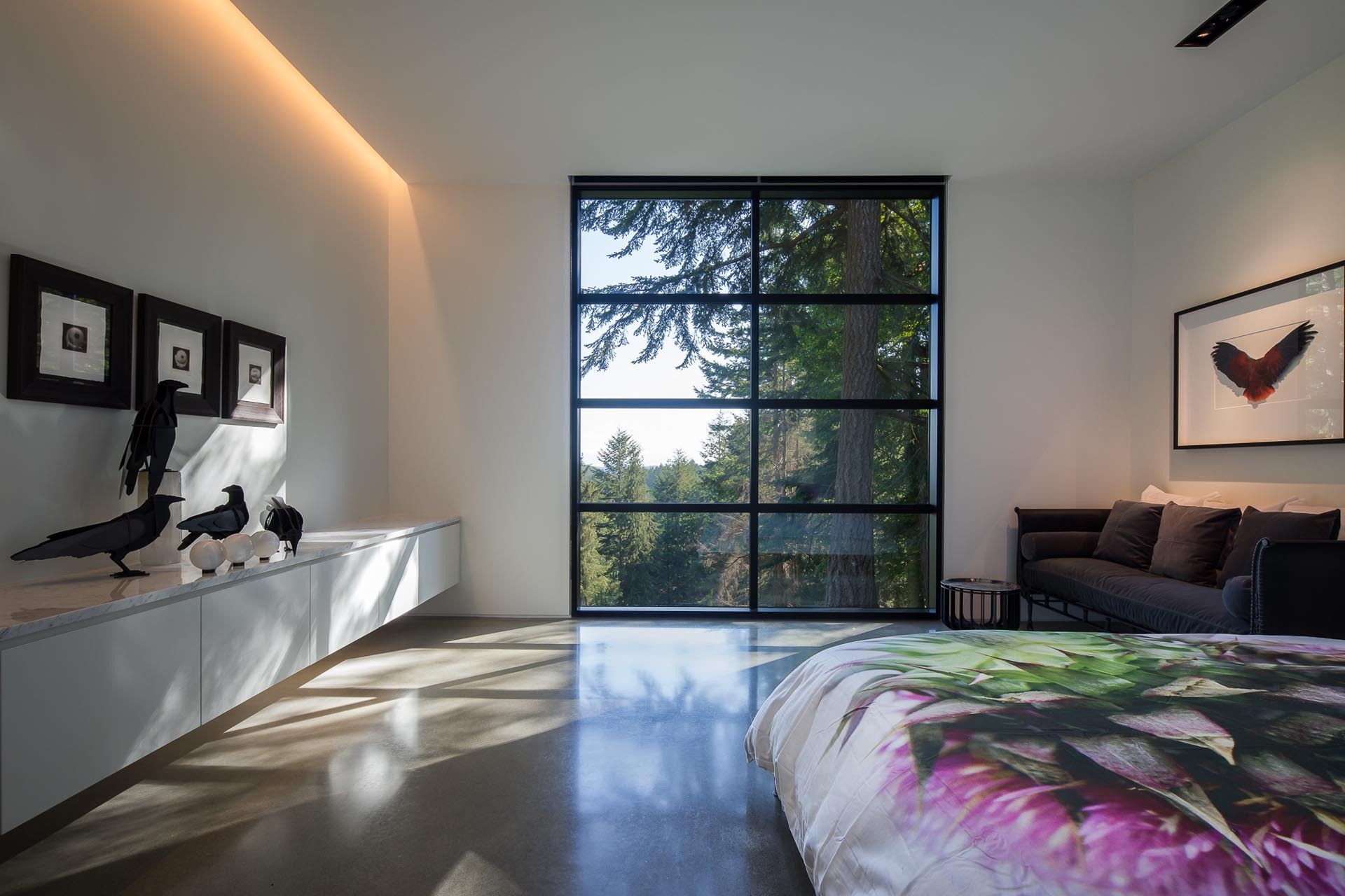 This modern bedroom features floor-to-ceiling black-framed windows, introducing contrast against the otherwise light interior. Hidden lighting adds a soft, indirect glow.