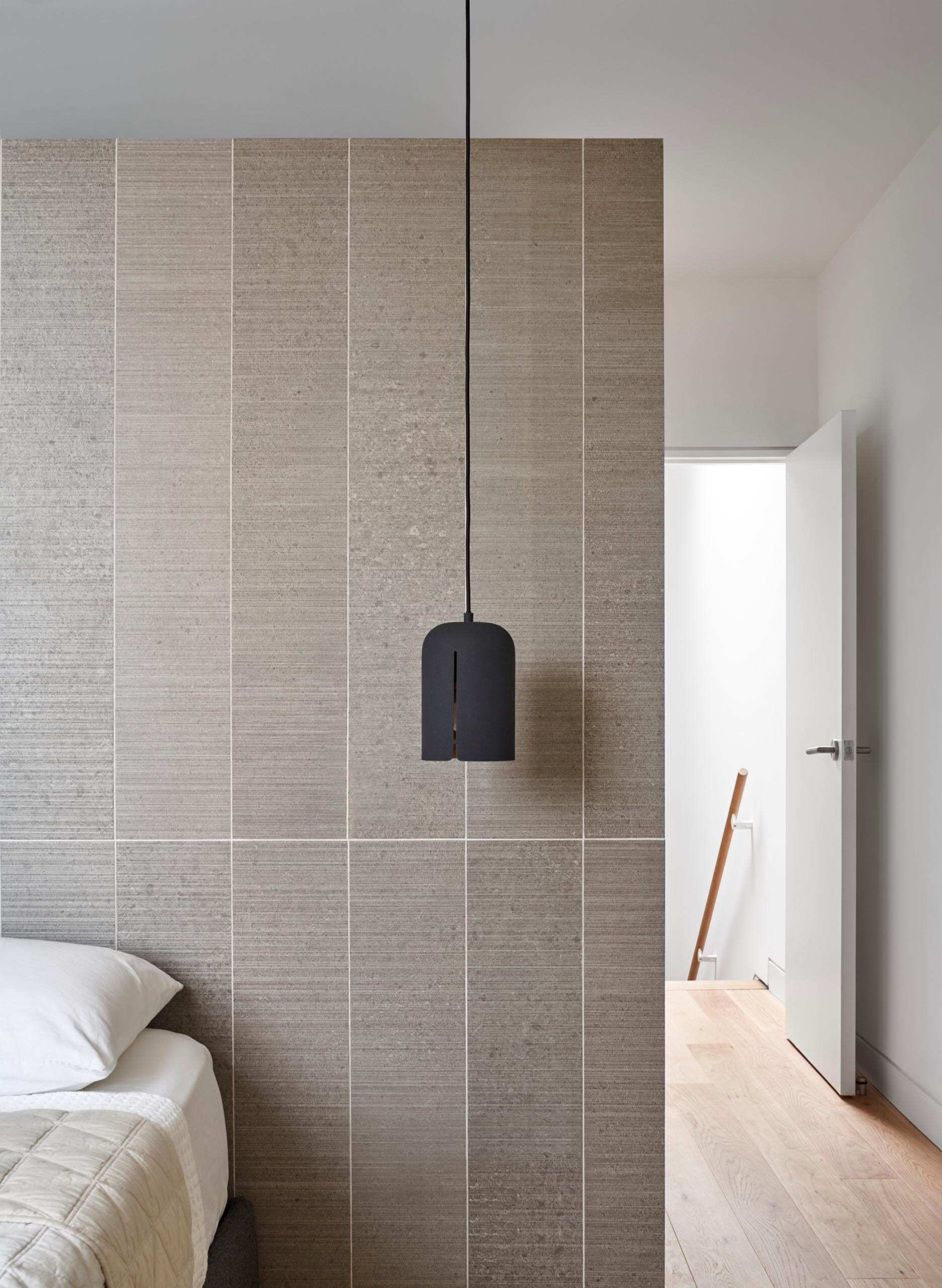 A matte black pendant light adds contrast in a minimalist bedroom with a soft accent wall backdrop.