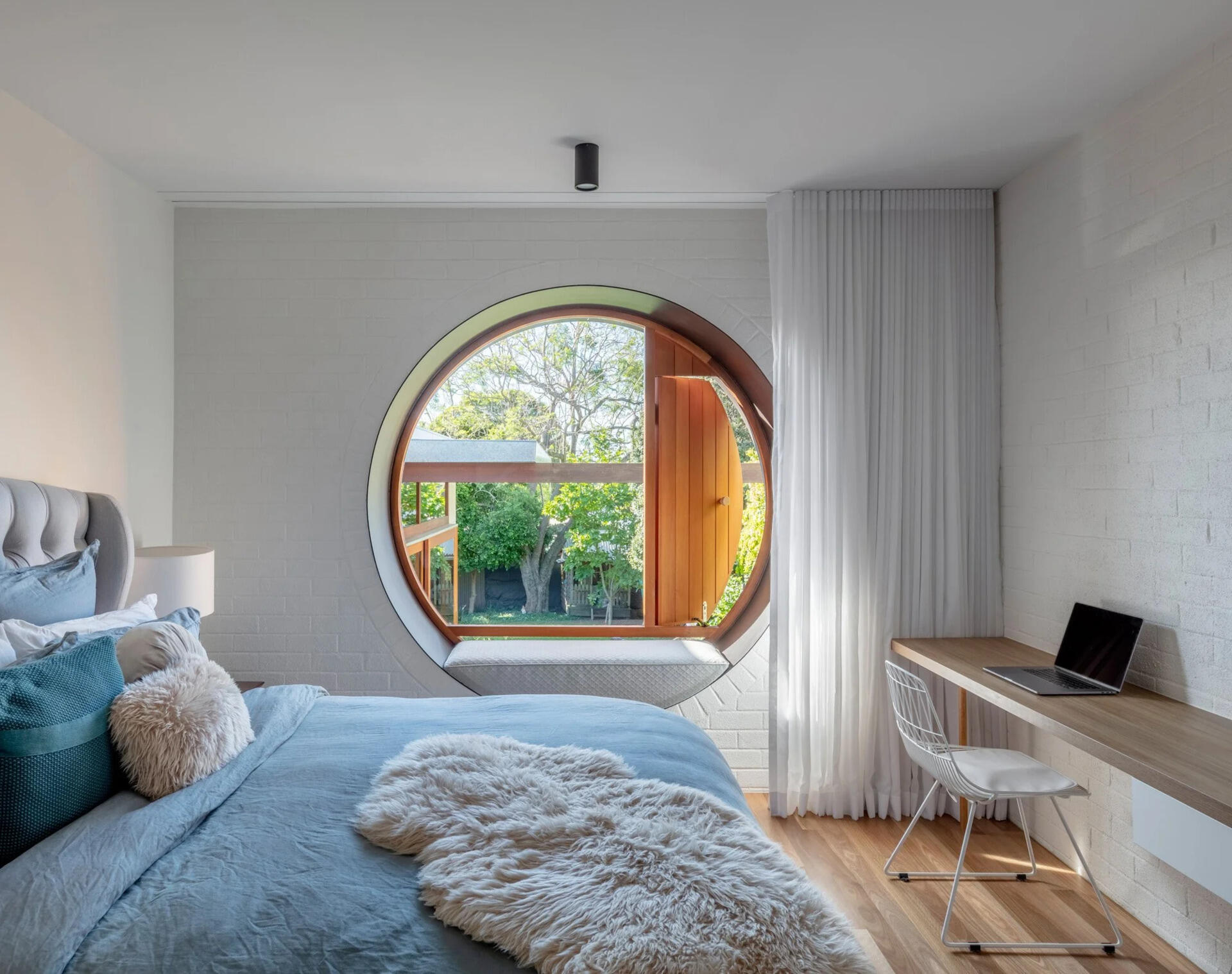 El dormitorio moderno cuenta con una ventana circular que enmarca el patio trasero y también funciona como zona de estar.