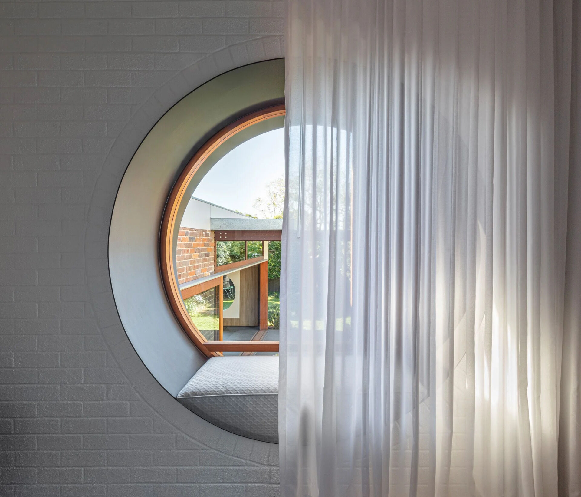 El dormitorio moderno cuenta con una ventana circular que enmarca el patio trasero y también funciona como zona de estar.