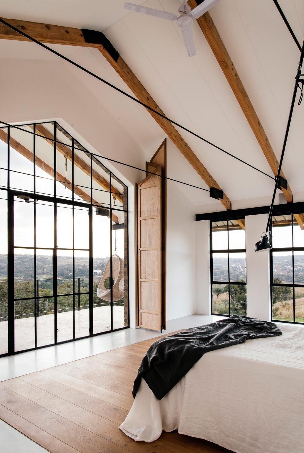 A minimal bedroom opens to tree canopy views, with shutters and overhangs controlling sunlight.