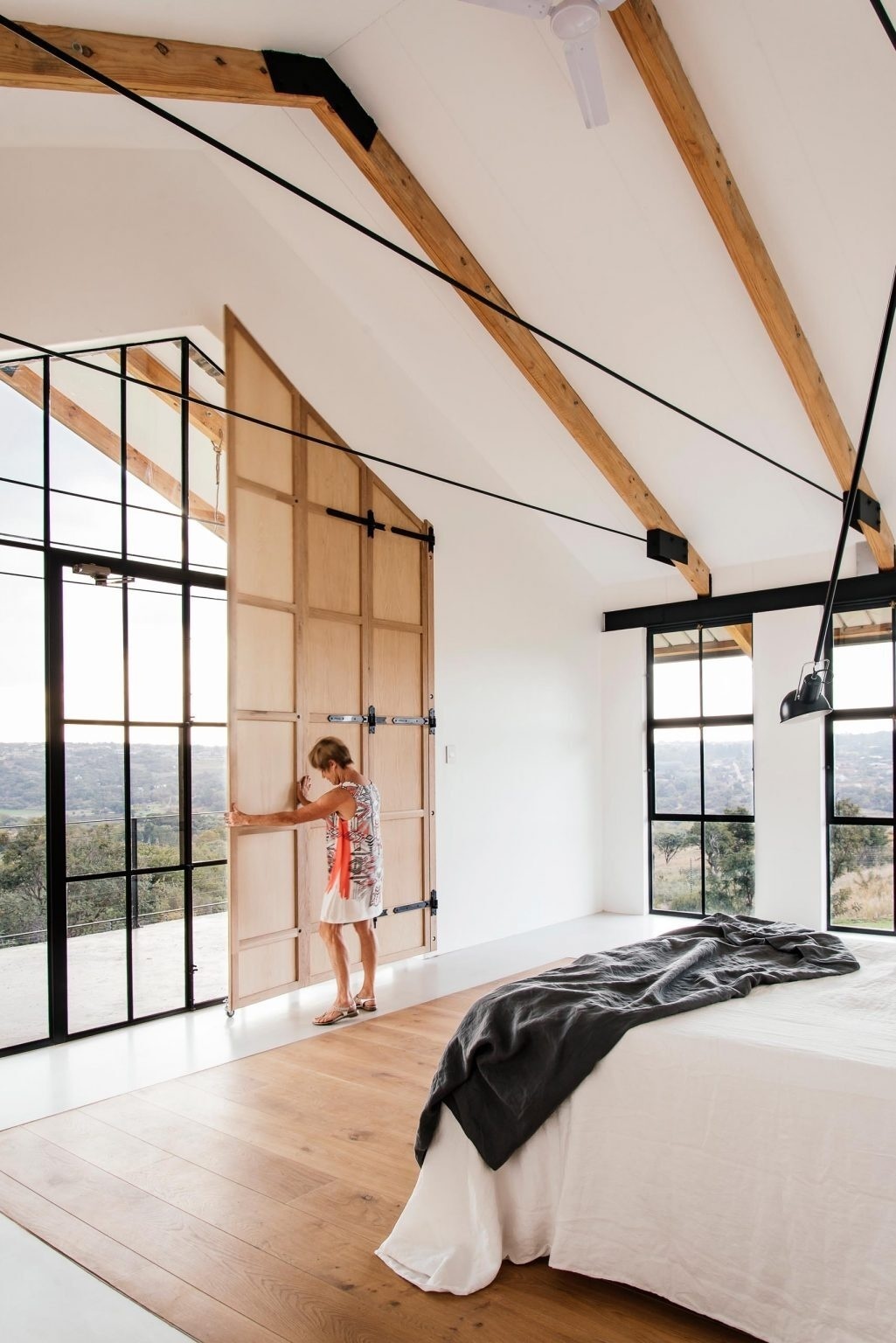 A minimal bedroom opens to tree canopy views, with shutters and overhangs controlling sunlight.