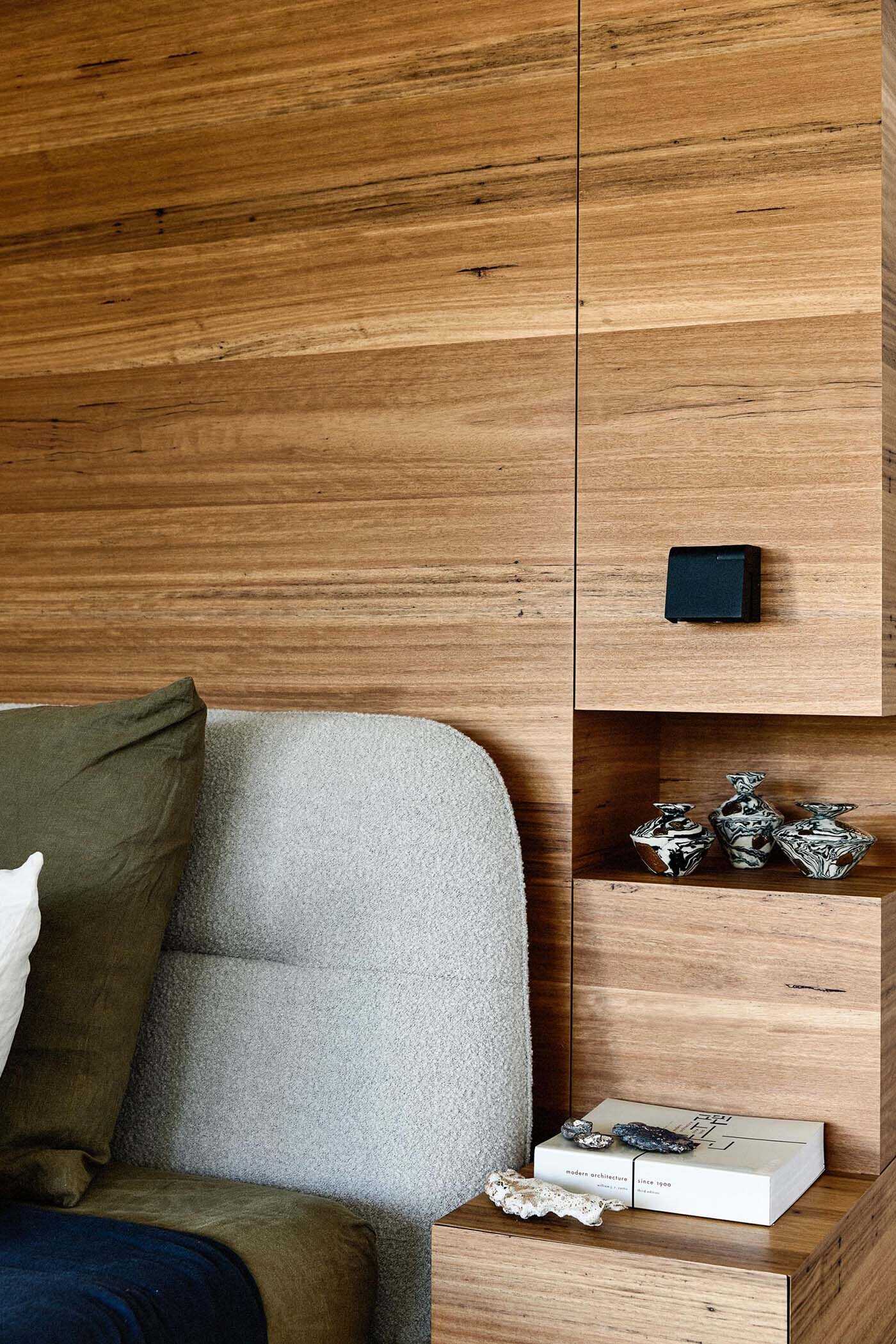 In this bathroom, a partial wood wall forms the backdrop to the bed, integrating bedside tables and shelving into a single feature.