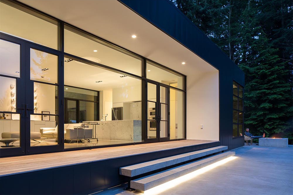 Black-framed doors open to a concrete terrace with a built-in fire pit, perfect for outdoor living.