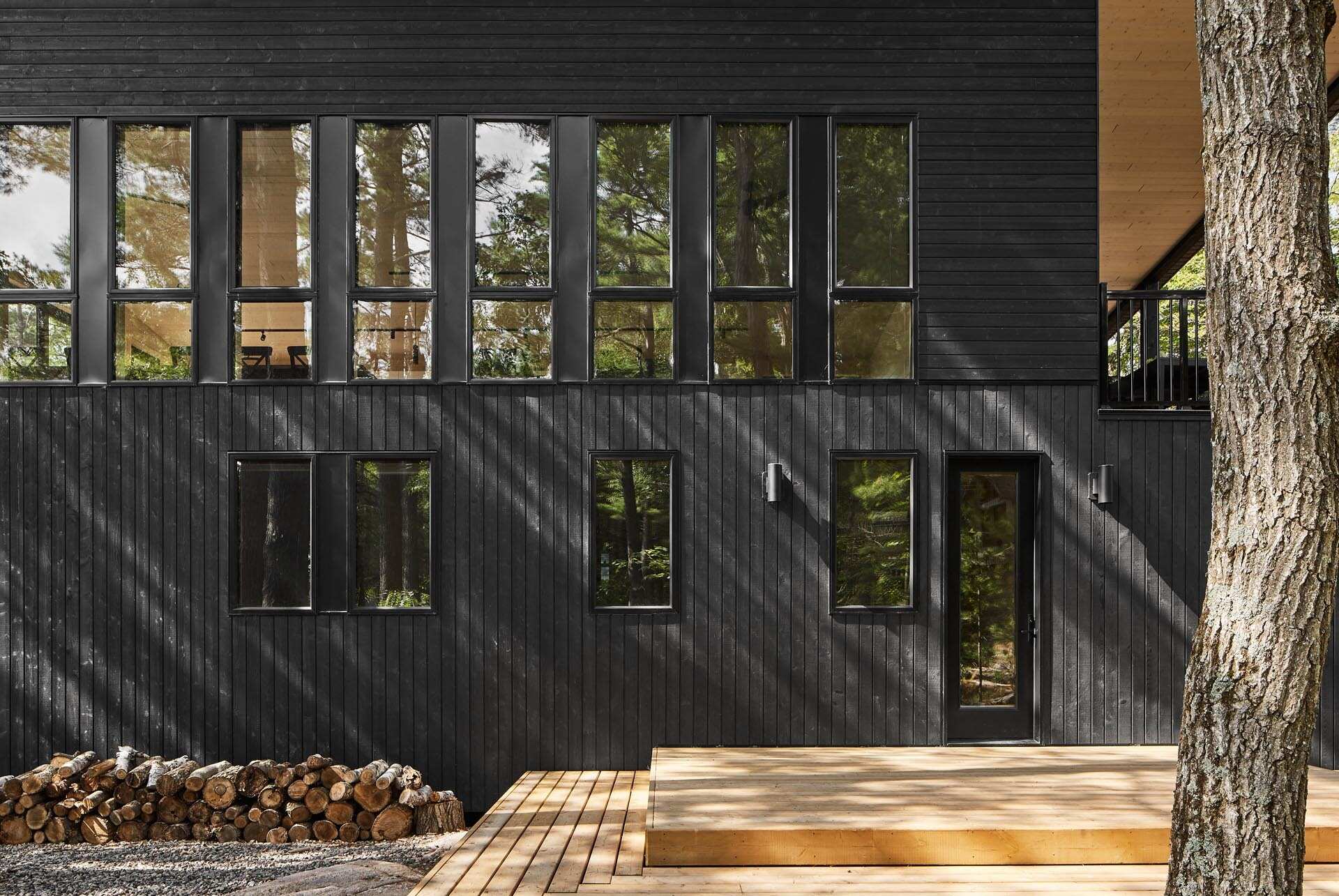 Black wood siding and matching window frames give this Muskoka cottage a bold yet subtle exterior that blends into the forest.