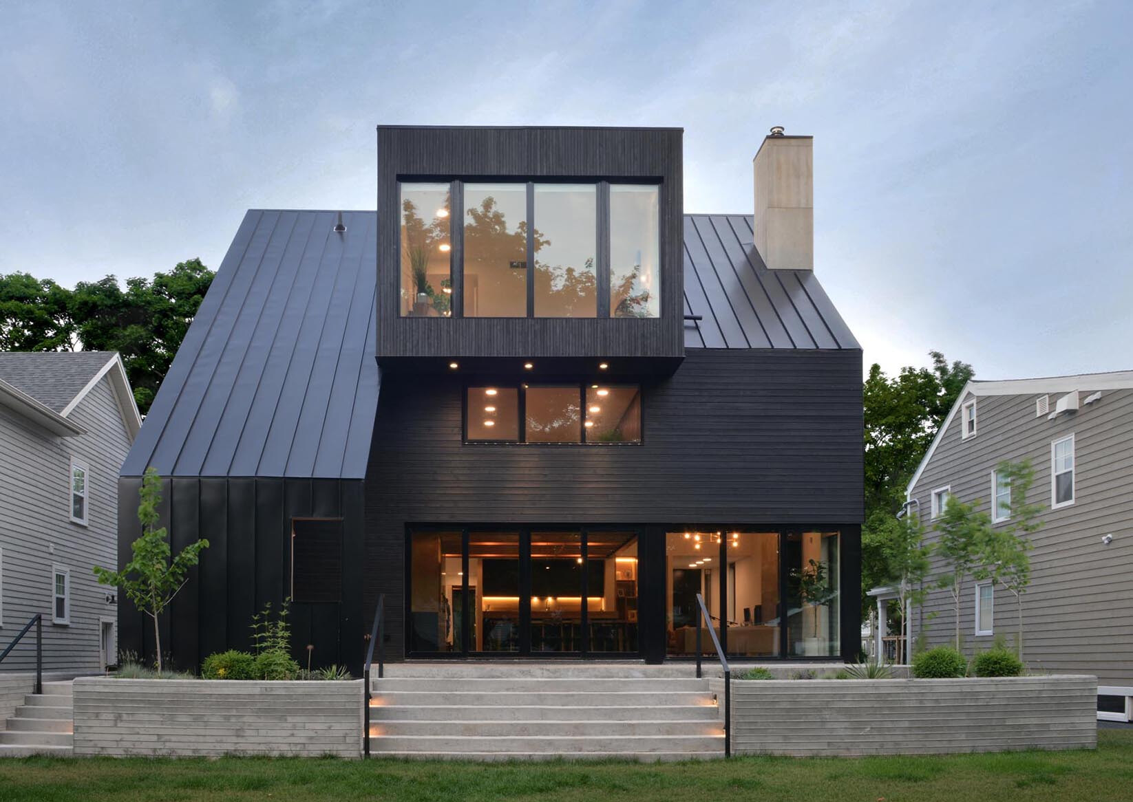 Esta casa negra combina un techo de metal con junta alzada con revestimiento de madera para crear profundidad y textura que cambian a lo largo del día.