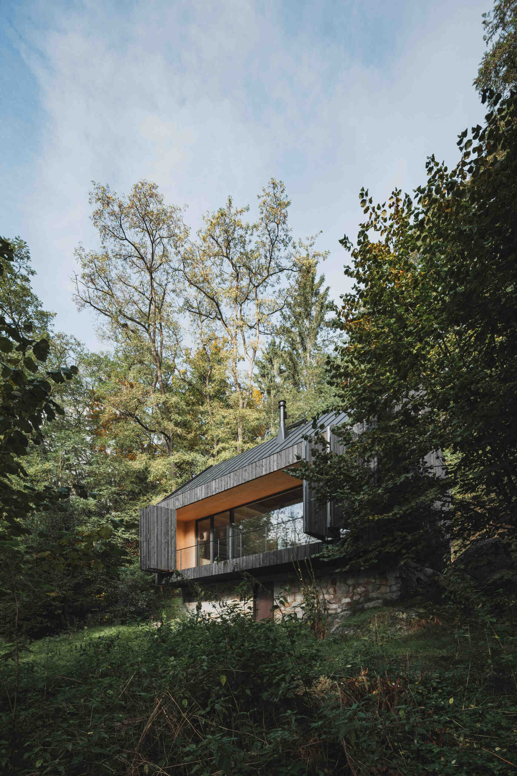 A small cabin in Prosecnice, Czech Republic rebuilt on its original stone base, opening up to peaceful views over the Sázava River.