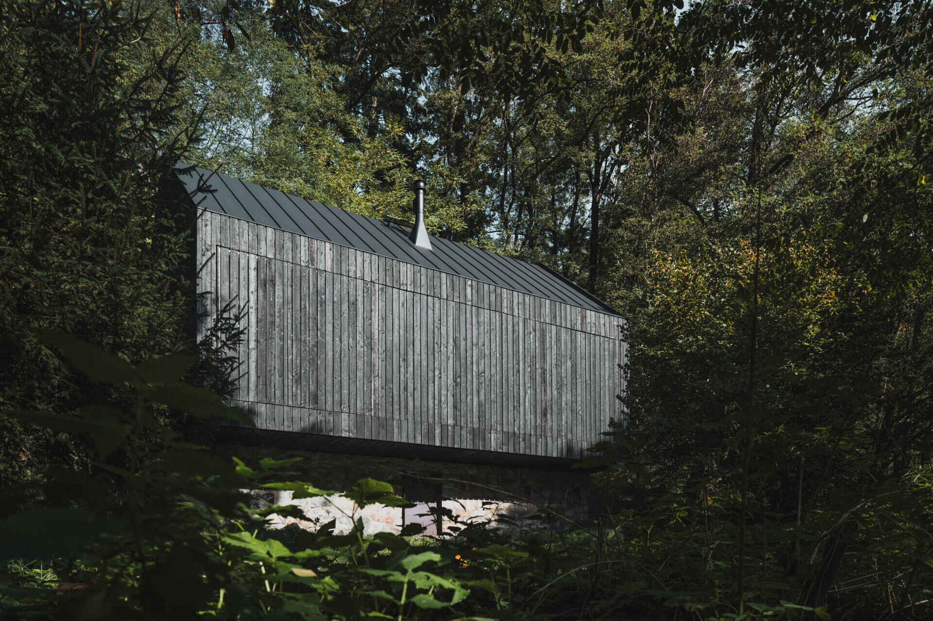 A small cabin in Prosecnice, Czech Republic rebuilt on its original stone base, opening up to peaceful views over the Sázava River.