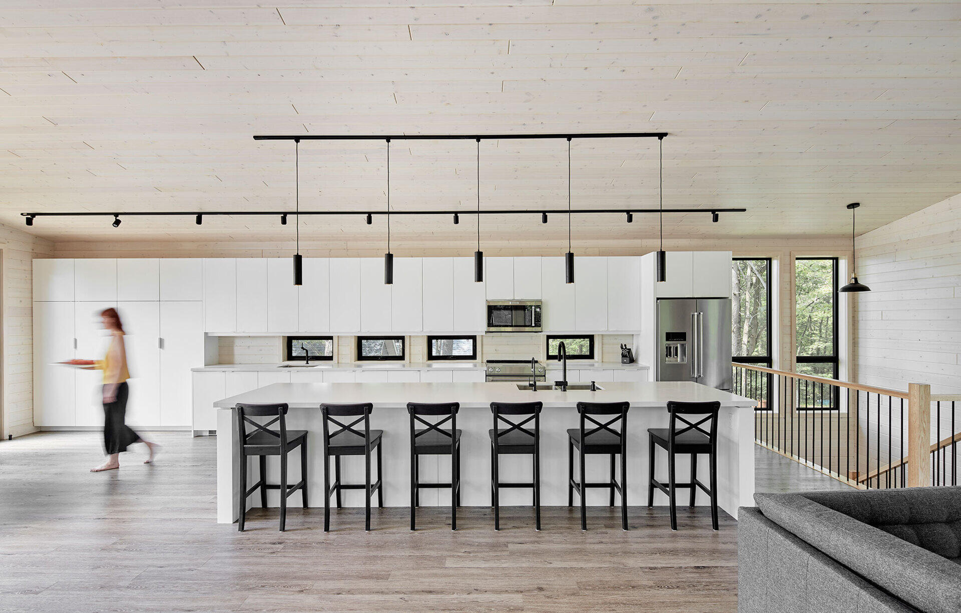 An open-plan upper level with a fireplace lounge, multiple dining tables, and a bold black-and-white kitchen designed for large family gatherings.