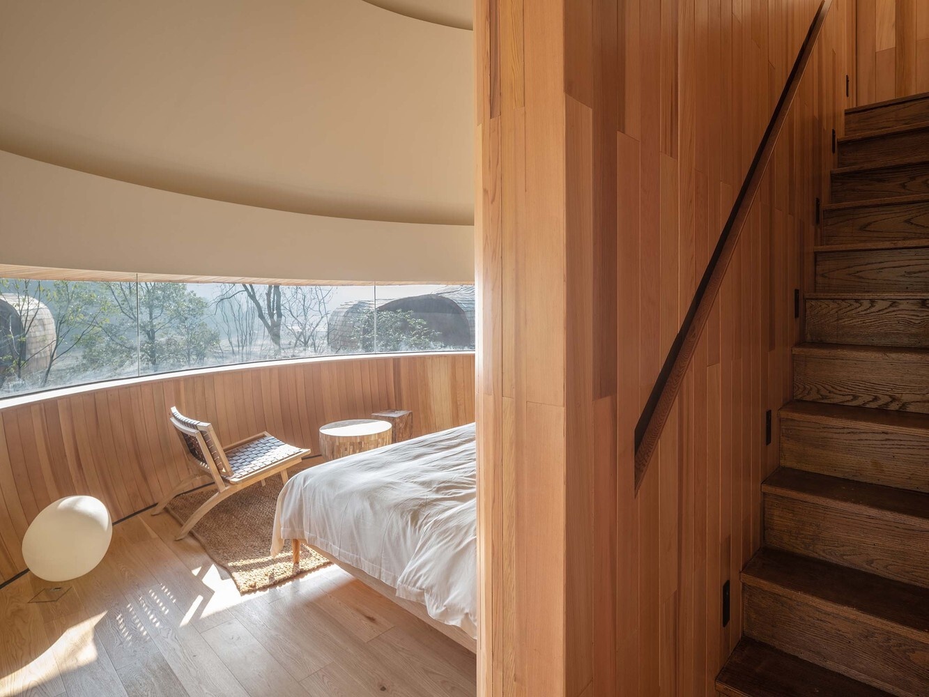 Curved panoramic windows wrap the bedroom, framing uninterrupted views of the surrounding pine forest.