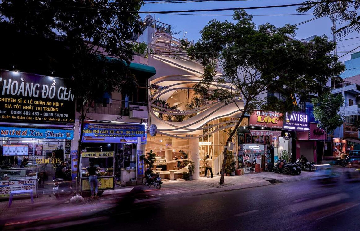 At night, hidden lighting brings this sculptural cafe facade to life, glowing through its curved steel layers.