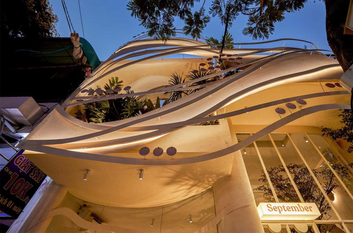 At night, hidden lighting brings this sculptural cafe facade to life, glowing through its curved steel layers.