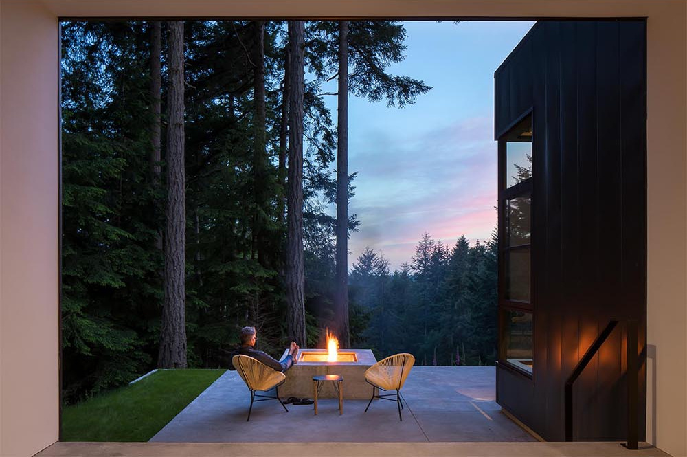 Black-framed doors open to a concrete terrace with a built-in fire pit, perfect for outdoor living.