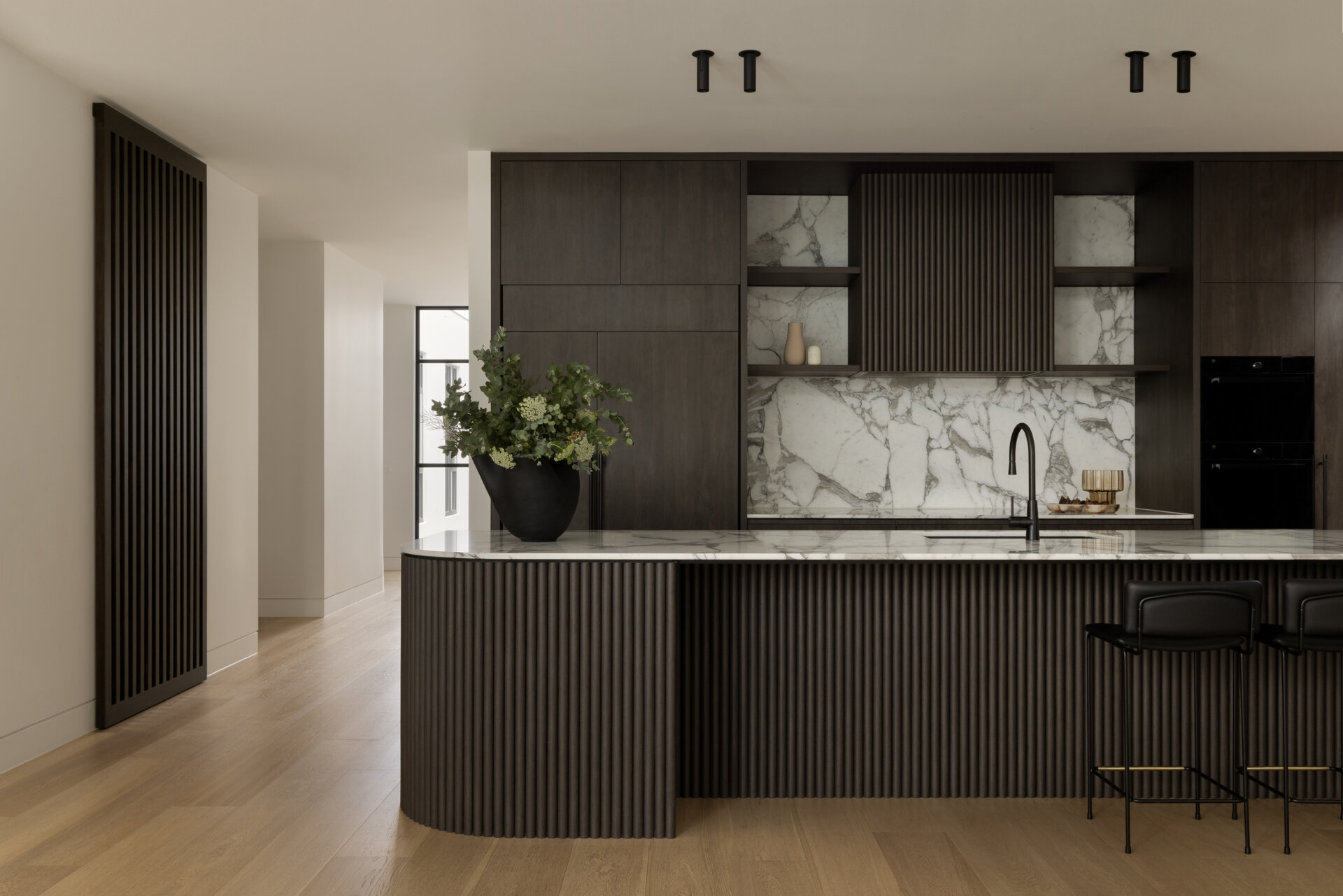 This kitchen, with its dark cabinets and rounded island, plays a central role in the home’s layout, designed to handle everything from daily meals to larger family events.