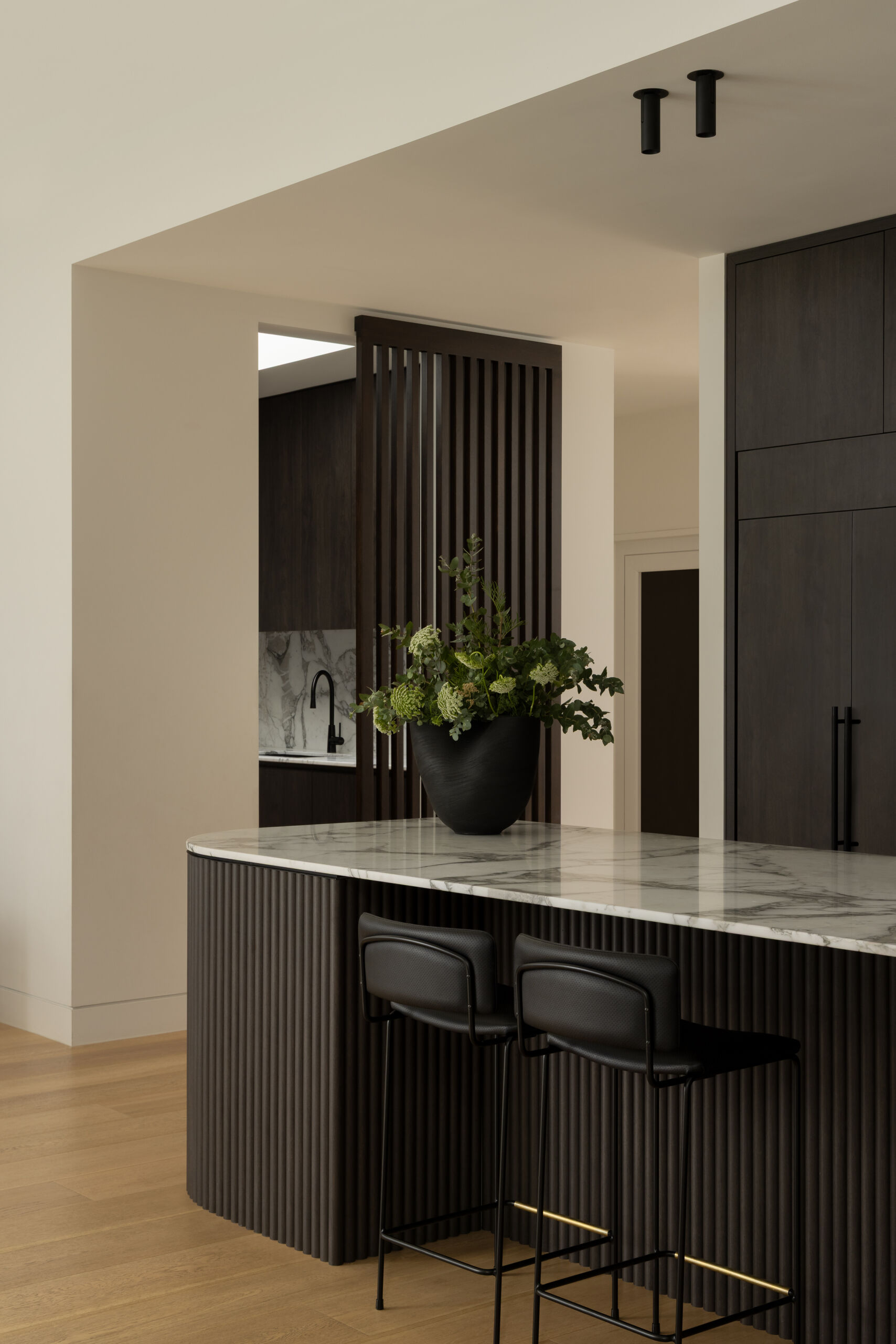 This kitchen, with its dark cabinets and rounded island, plays a central role in the home’s layout, designed to handle everything from daily meals to larger family events.