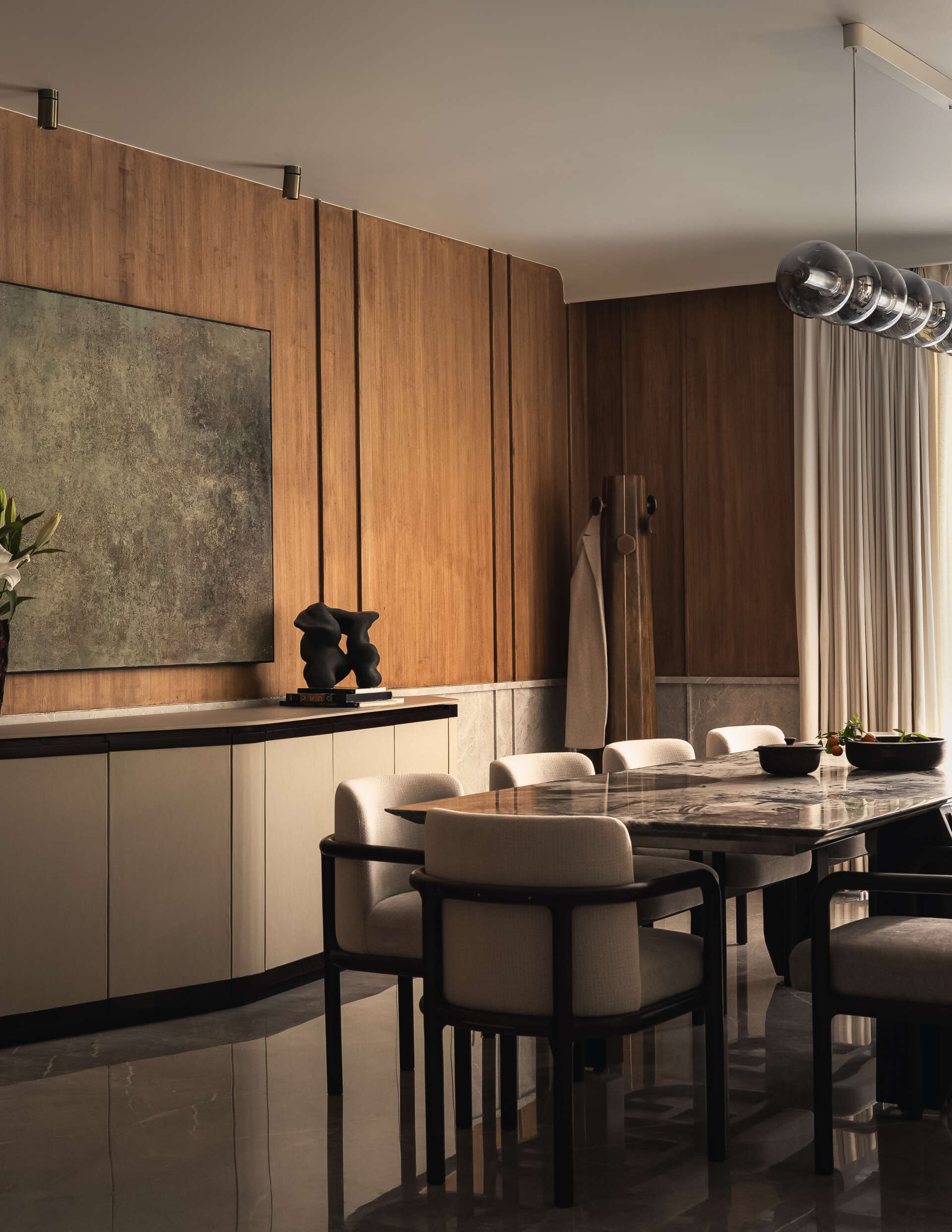 The dining space sits comfortably within the overall flow of the home. It doesn’t try to stand apart, instead working with the same soft tones and material palette seen throughout. A large 10-seater table with lighting overhead draws attention, while the sideboard blends into its surrounds.