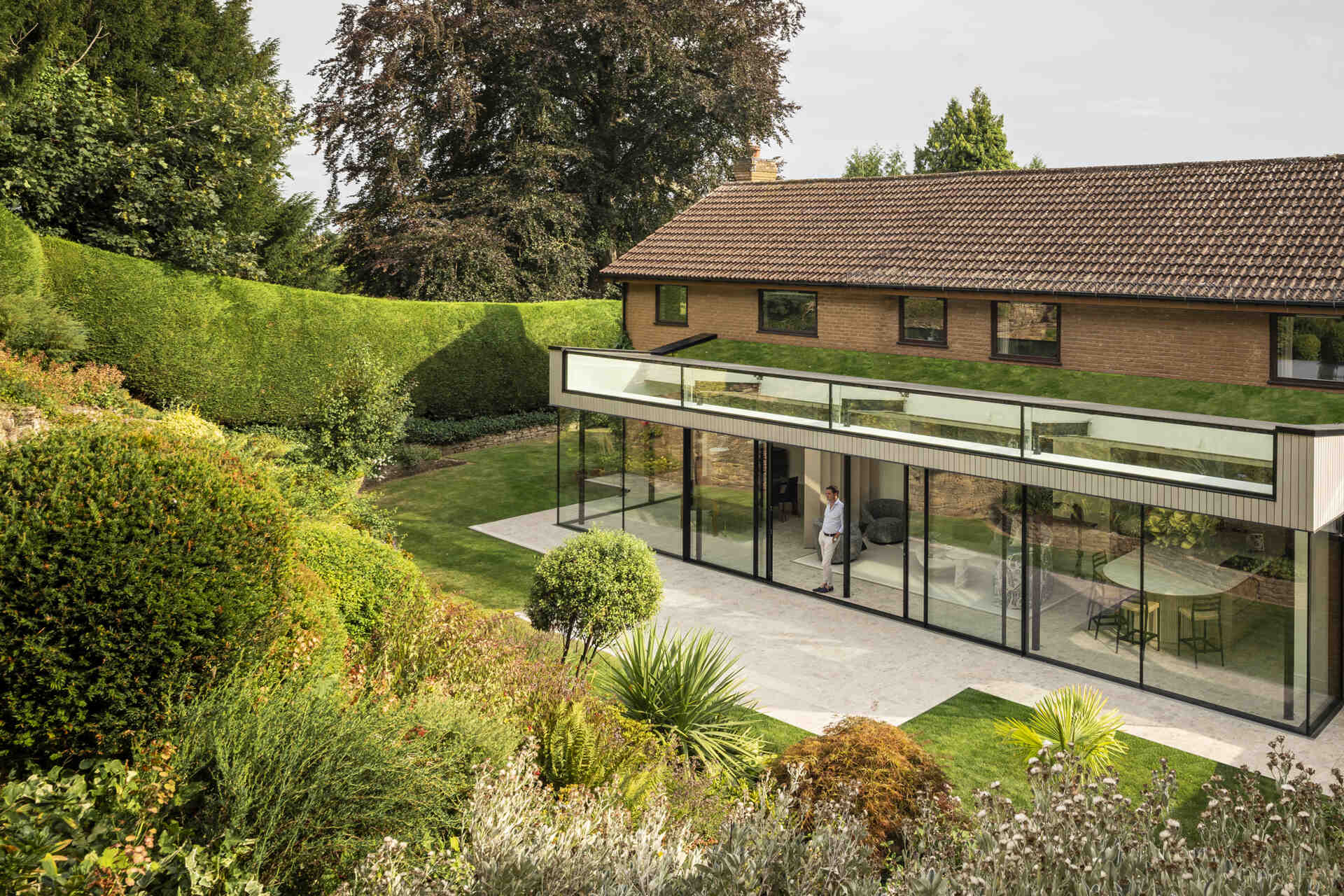 This rear extension with a green roof, uses full-height glazing to connect the kitchen and living areas directly to a sloping garden, creating a seamless indoor-outdoor feel.