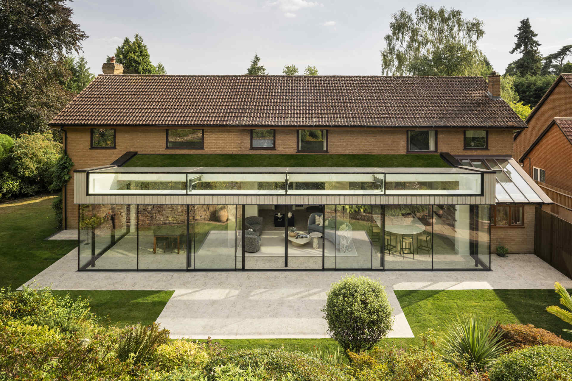 This rear extension with a green roof, uses full-height glazing to connect the kitchen and living areas directly to a sloping garden, creating a seamless indoor-outdoor feel.