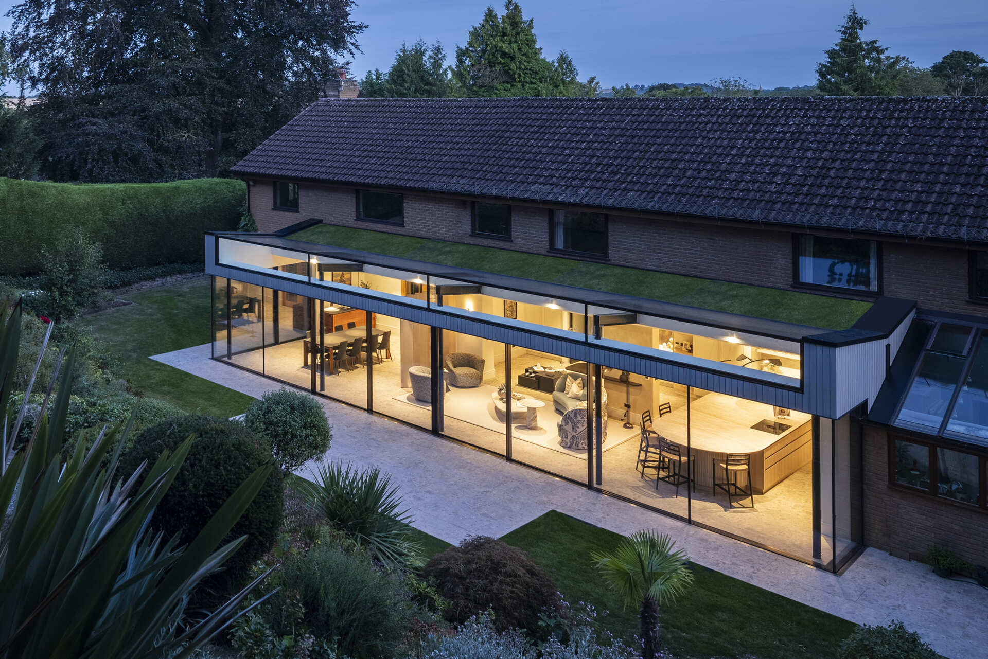 This rear extension with a green roof, uses full-height glazing to connect the kitchen and living areas directly to a sloping garden, creating a seamless indoor-outdoor feel.