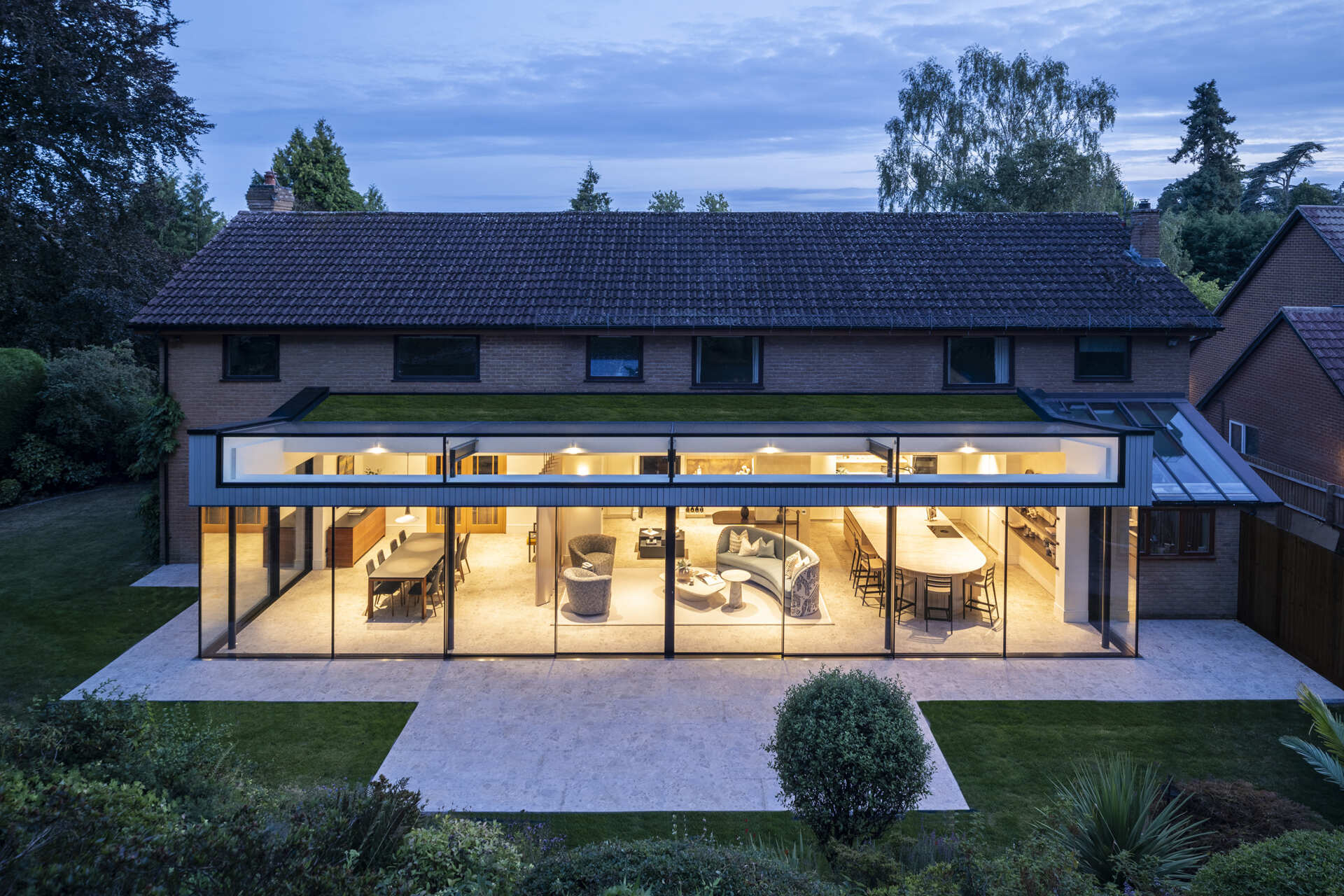 This rear extension uses full-height glazing to connect the kitchen and living areas directly to a sloping garden, creating a seamless indoor-outdoor feel.