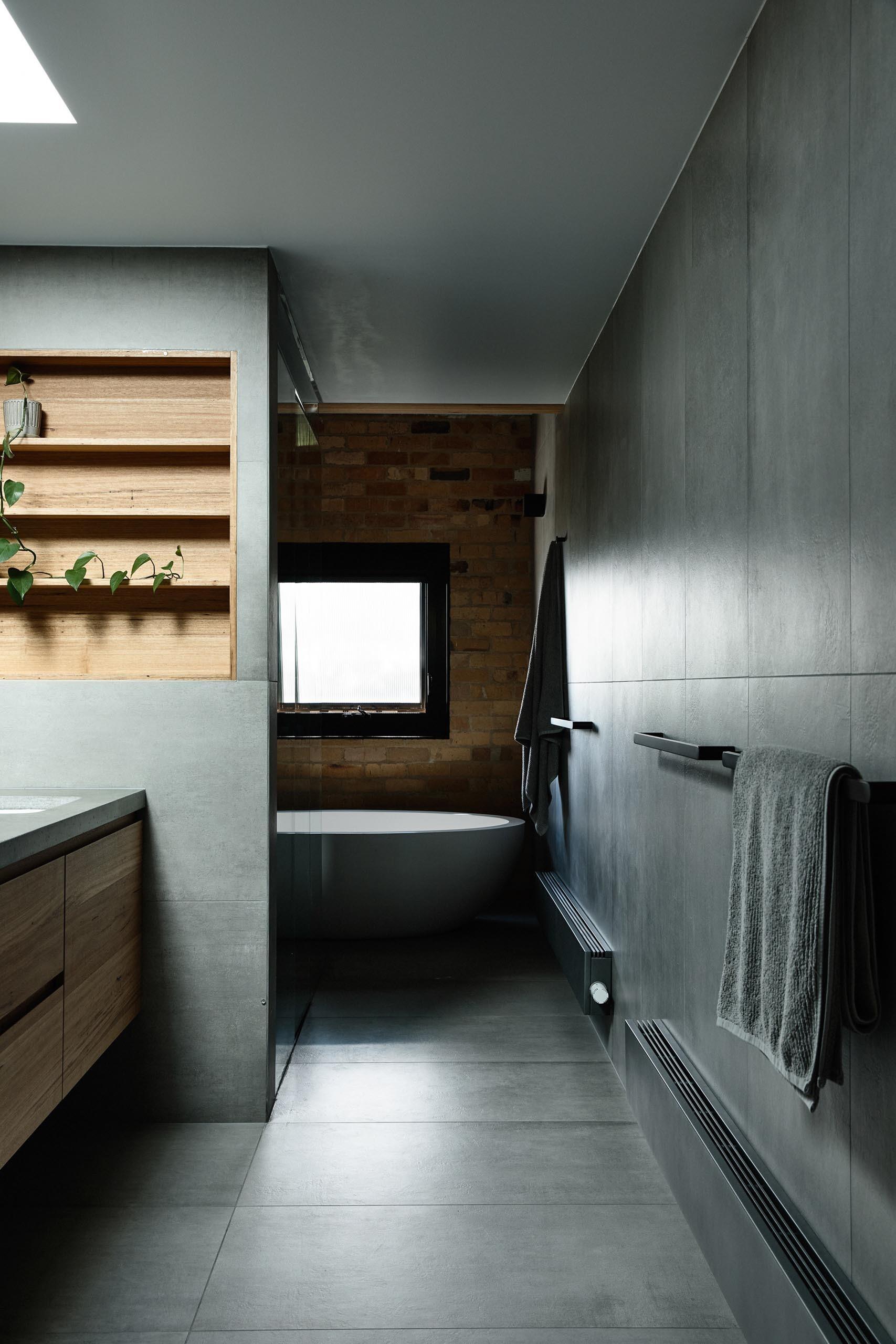 This modern bathroom uses grey tones with a wood-lined niche, metallic tiles, and a freestanding bathtub.