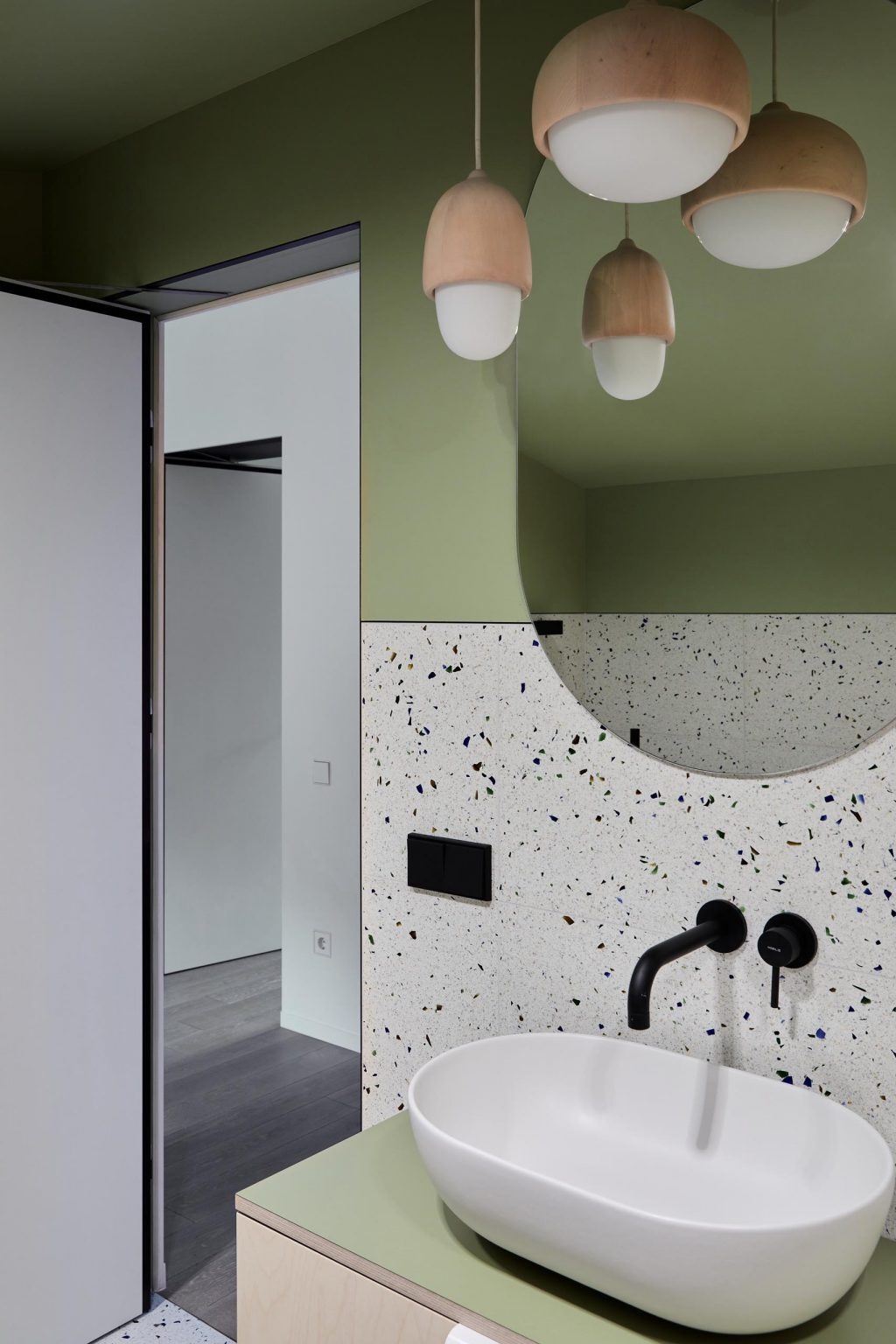 This bathroom combines matte green walls and ceiling with terrazzo surfaces and wood pendant lights, creating a layered material palette.