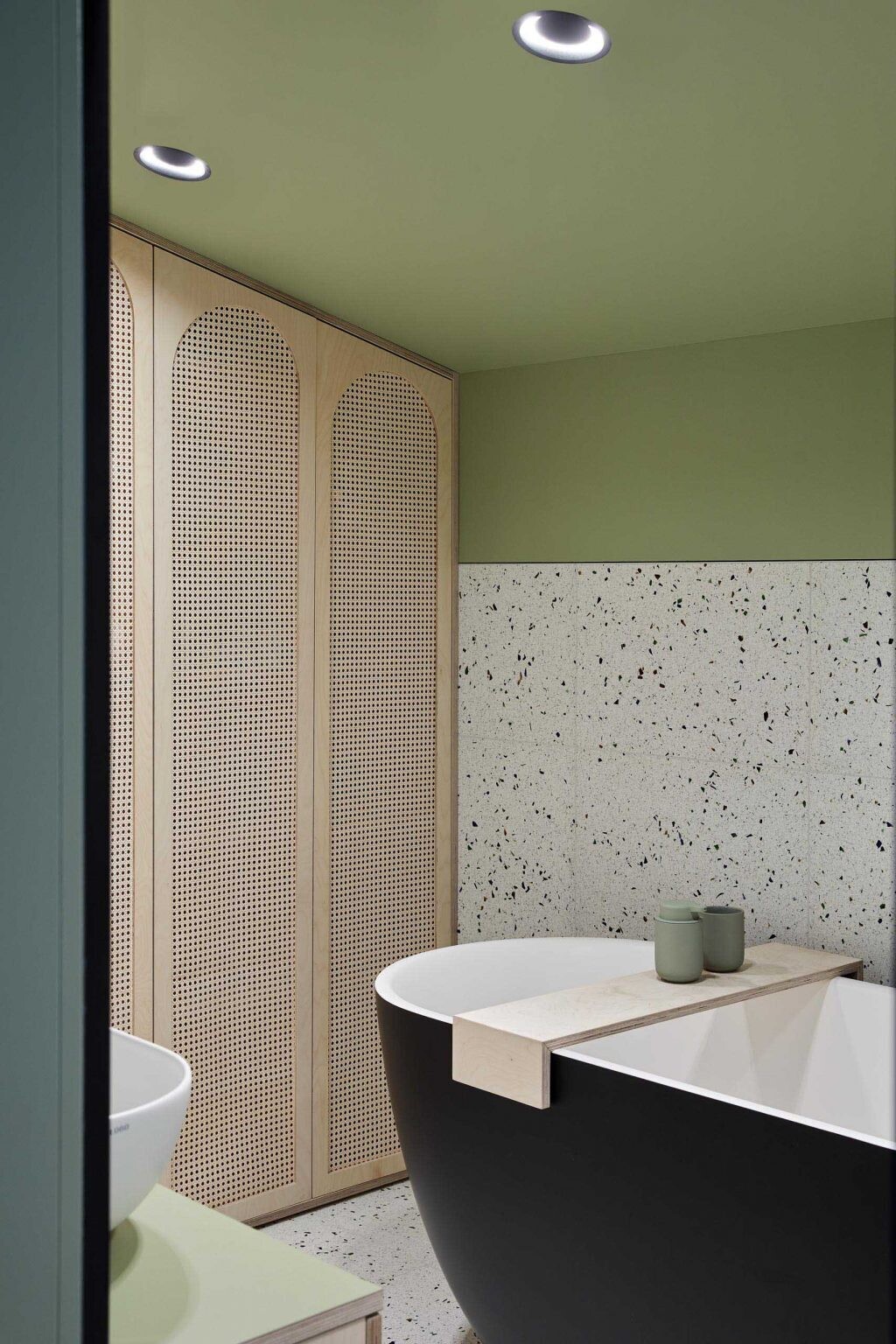 This bathroom combines matte green walls and ceiling with terrazzo surfaces and wood pendant lights, creating a layered material palette.