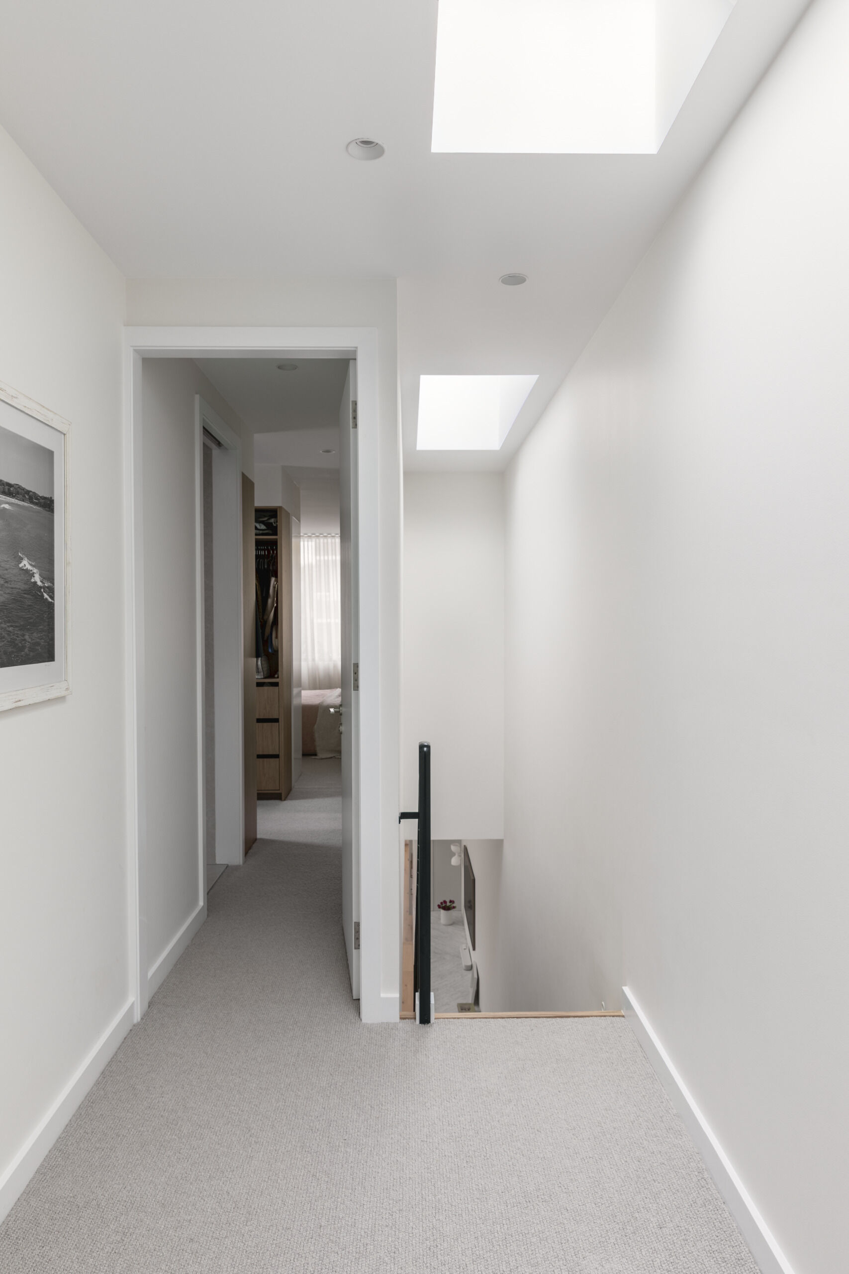 Skylights and large openings throughout the home, like above the staircase, draw natural light deep into the interior, highlighting timber, stone, and textured finishes that add warmth without overpowering the neutral palette.