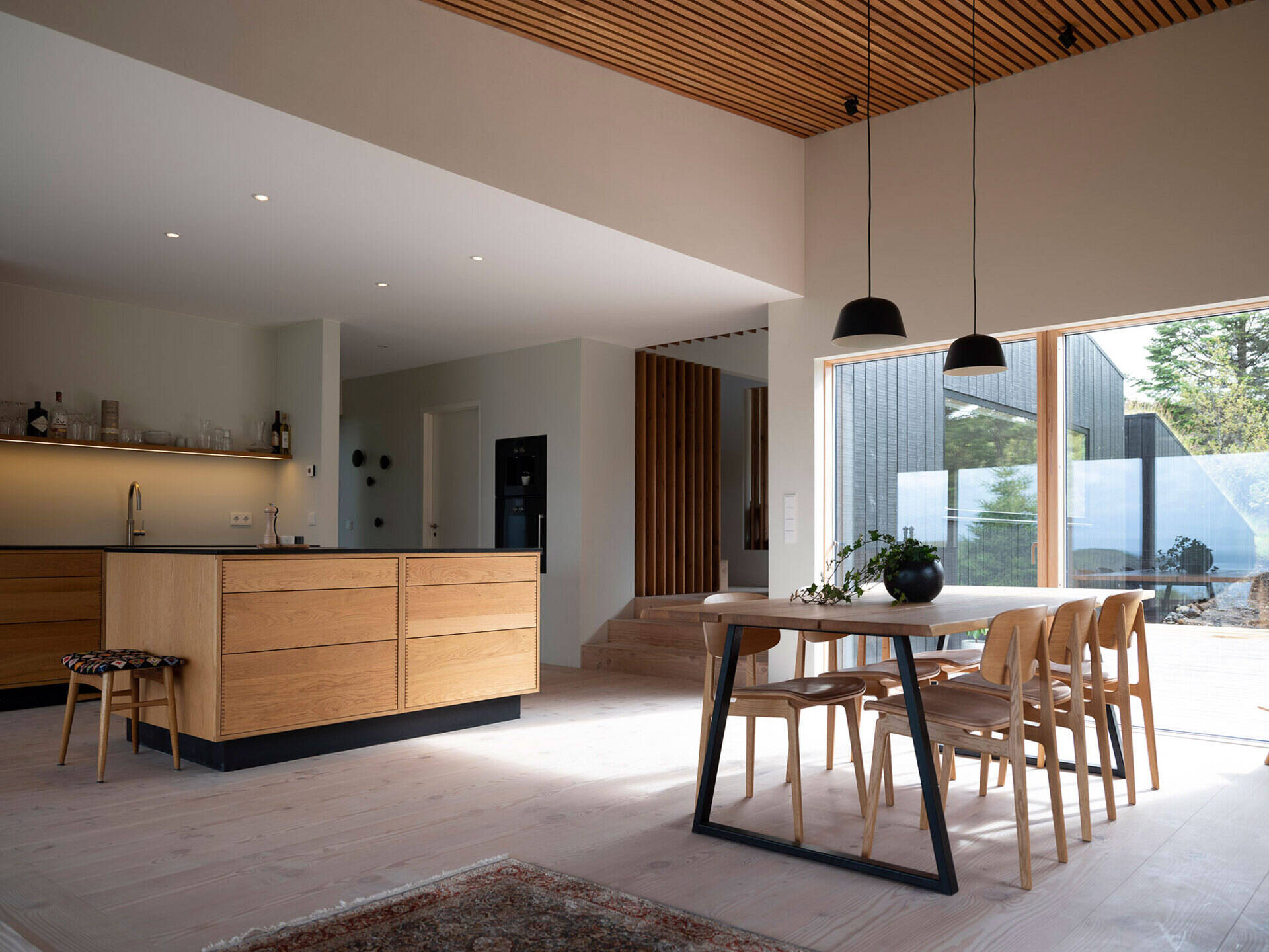 An open kitchen and dining area combines black accents with a warm wood slat ceiling and a sleek fireplace.