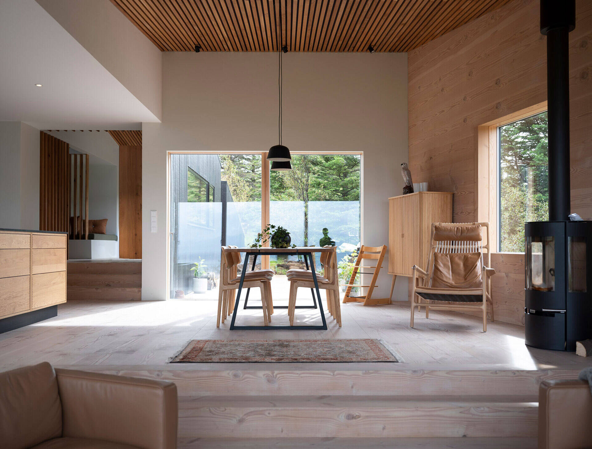 An open kitchen and dining area combines black accents with a warm wood slat ceiling and a sleek fireplace.