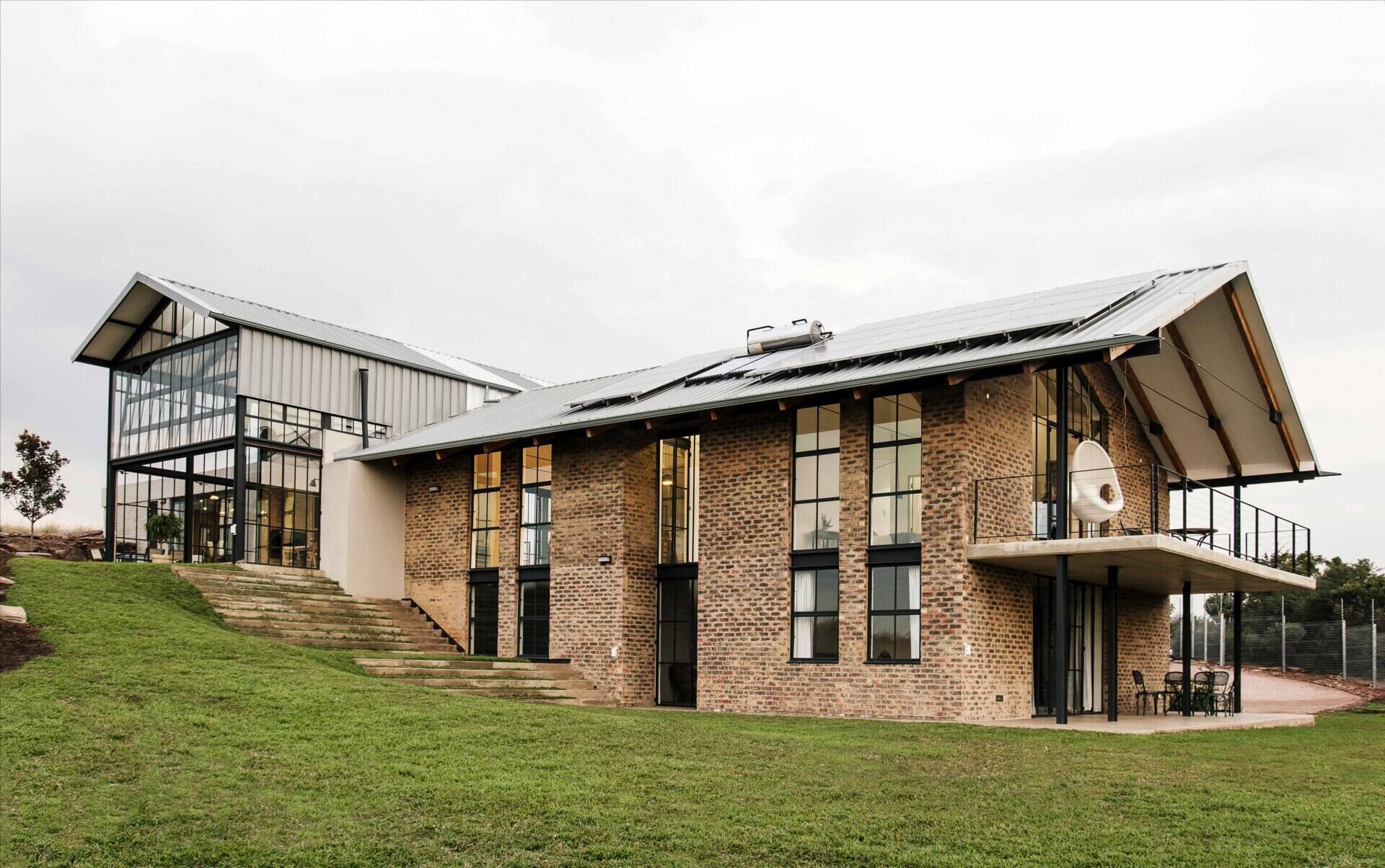 Cement-washed brick, steel, and concrete create a low-maintenance exterior with a strong, modern edge. A double-height conservatory with openable walls and a glass floor becomes the heart of this light-filled home.