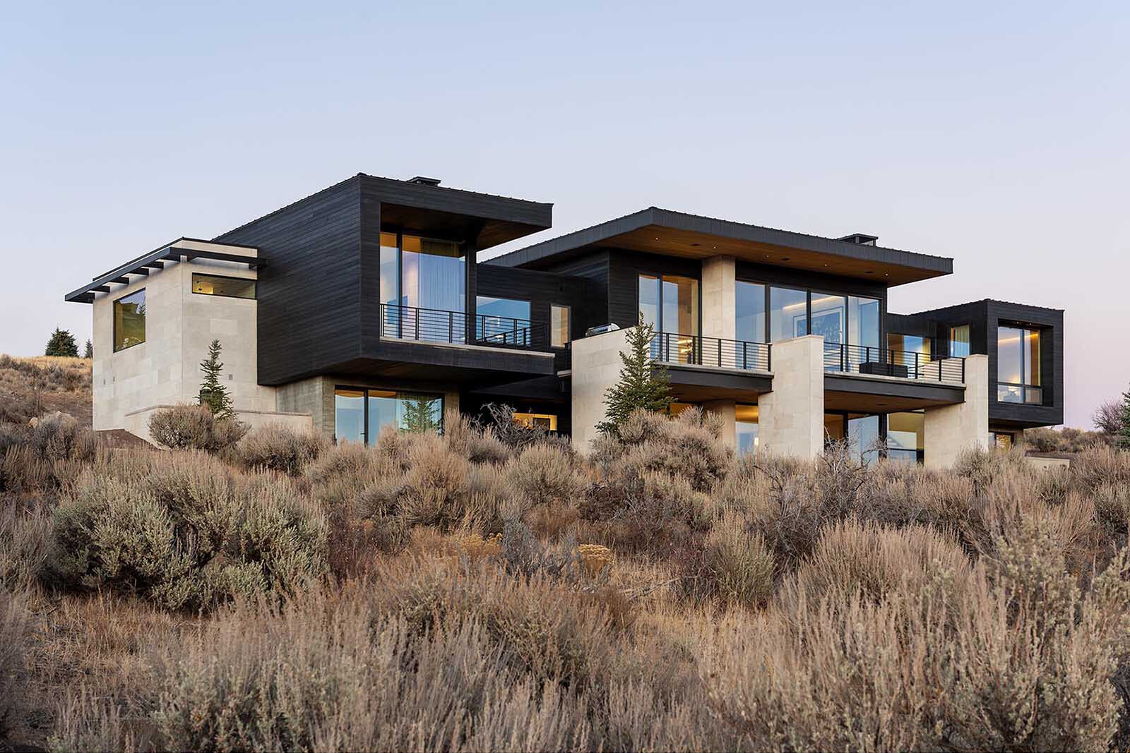 Modern mountain home exterior with black siding, exposed concrete, and a glass entry offering a preview of the interiors.
