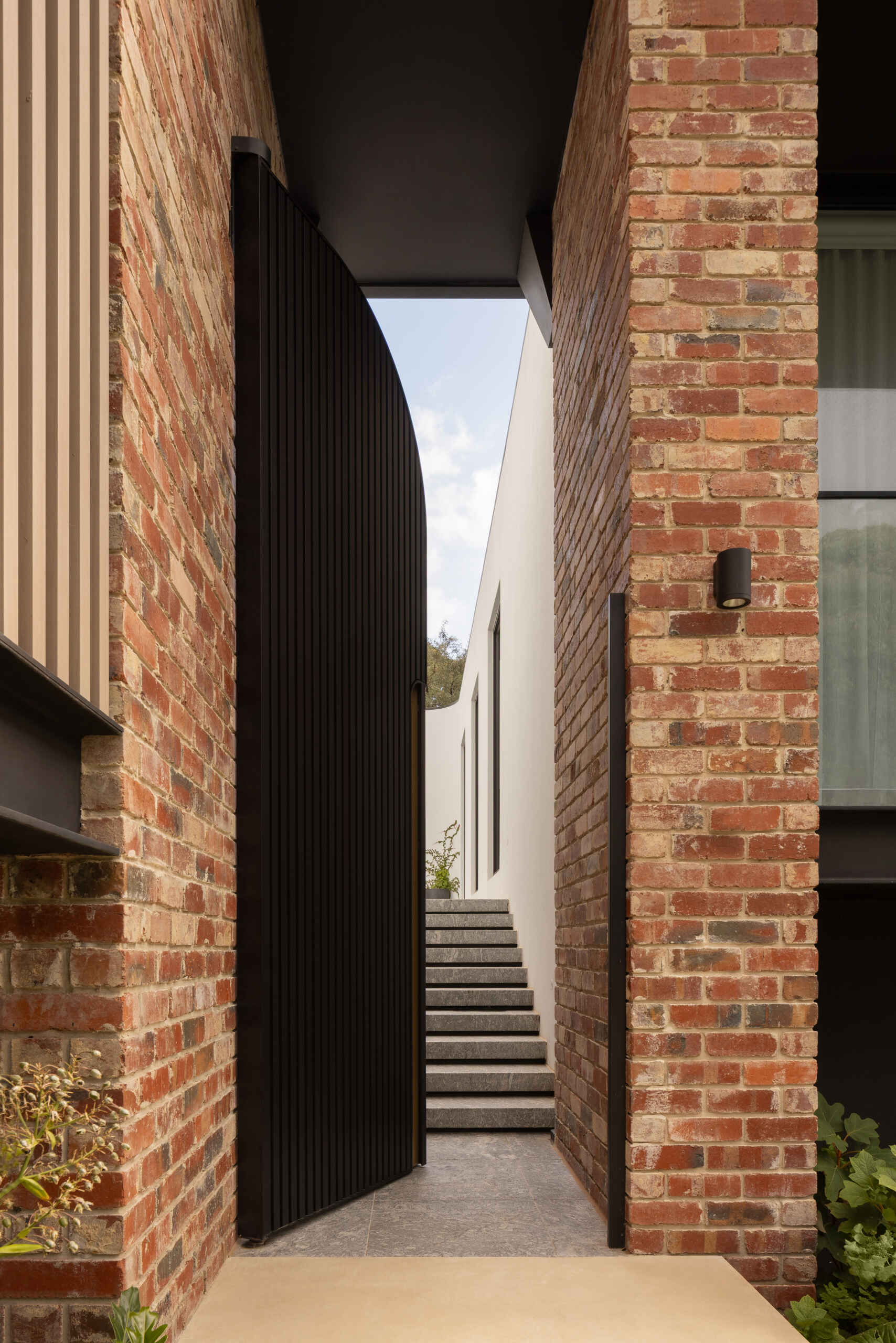 The journey begins with steps that lead to a large metal courtyard door. Passing through it introduces a slower pace, where movement becomes intentional and the transition into the home feels defined and memorable. The use of reclaimed clinker bricks ties the home back to its past, while also grounding it within the established character of the area.