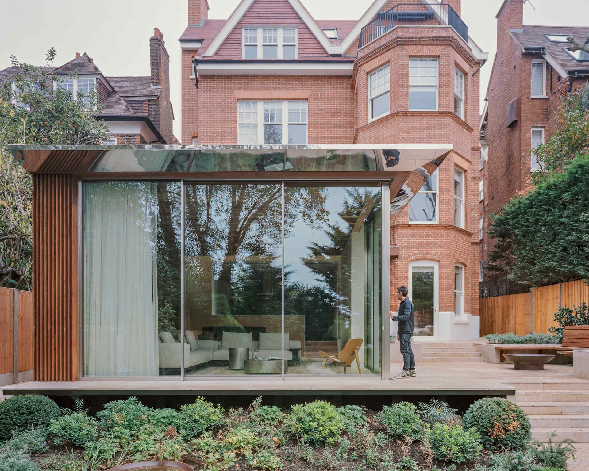 This cascading extension wrapped in iroko timber and topped with a reflective roof blends structure and greenery in a striking way.