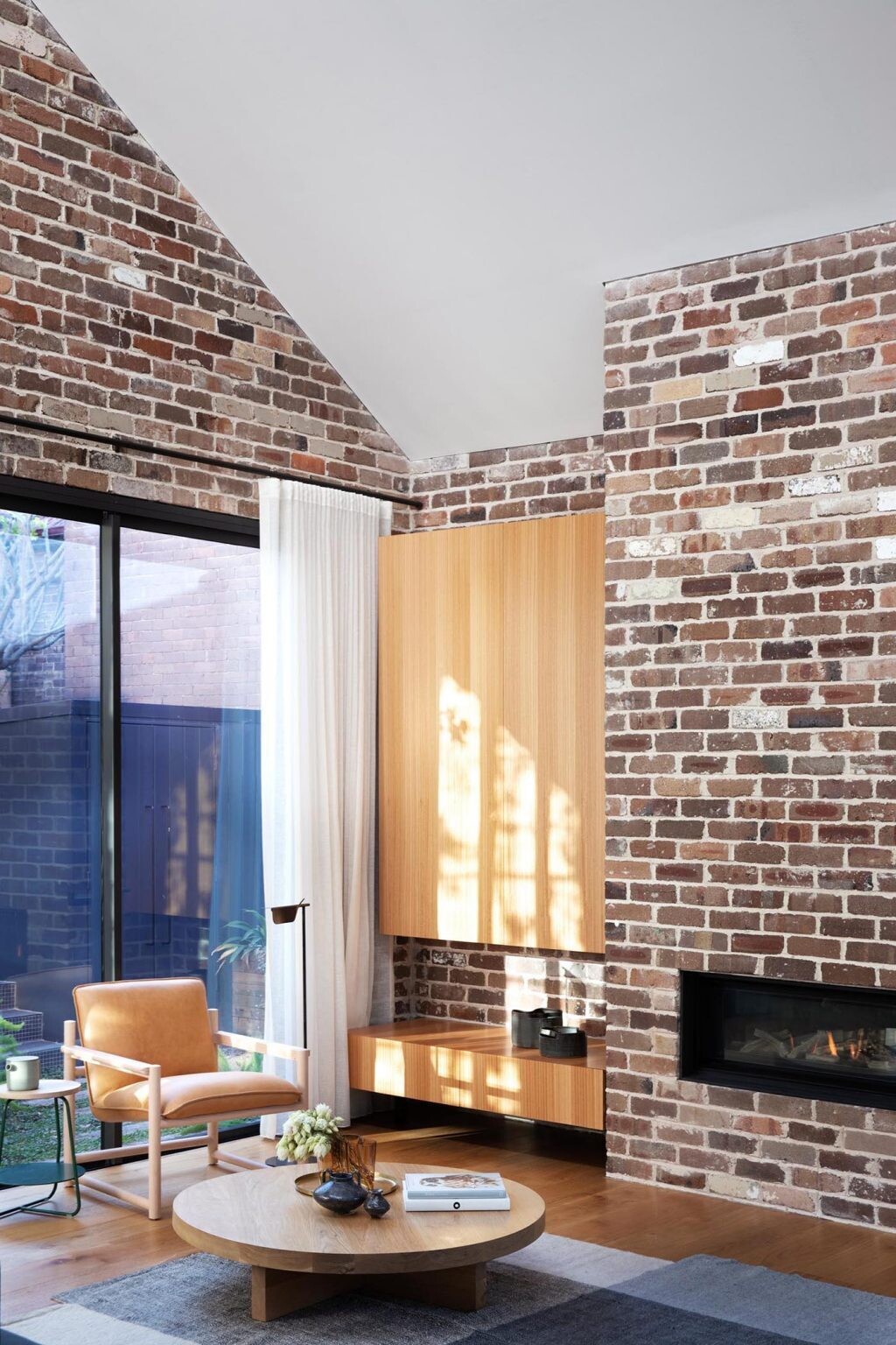 An open-plan living space combines a brick fireplace, custom wood cabinetry, and clean lines for a warm modern interior.